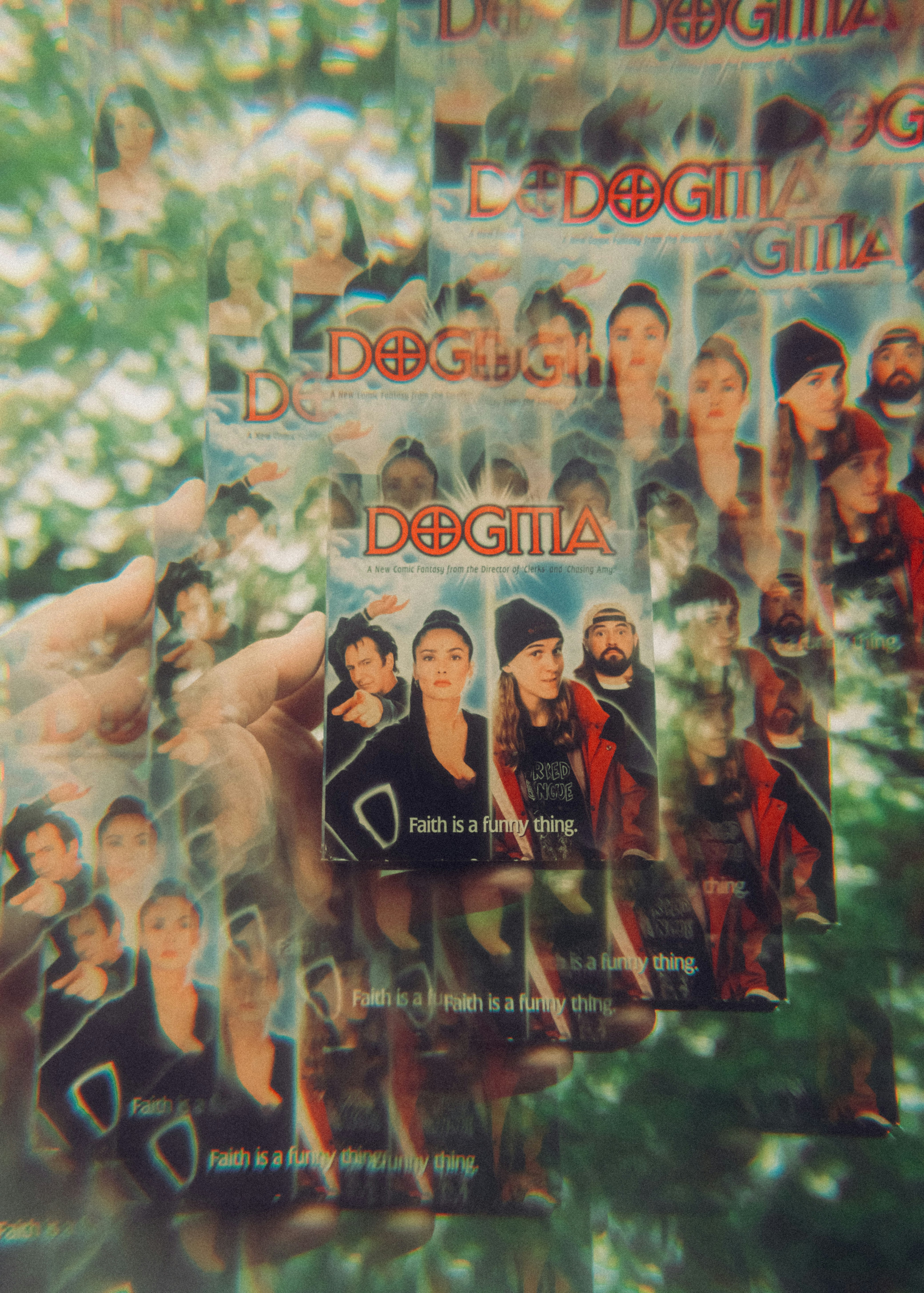 Mão segurando uma caixa de DVD "dogma" com efeito caleidoscópico.