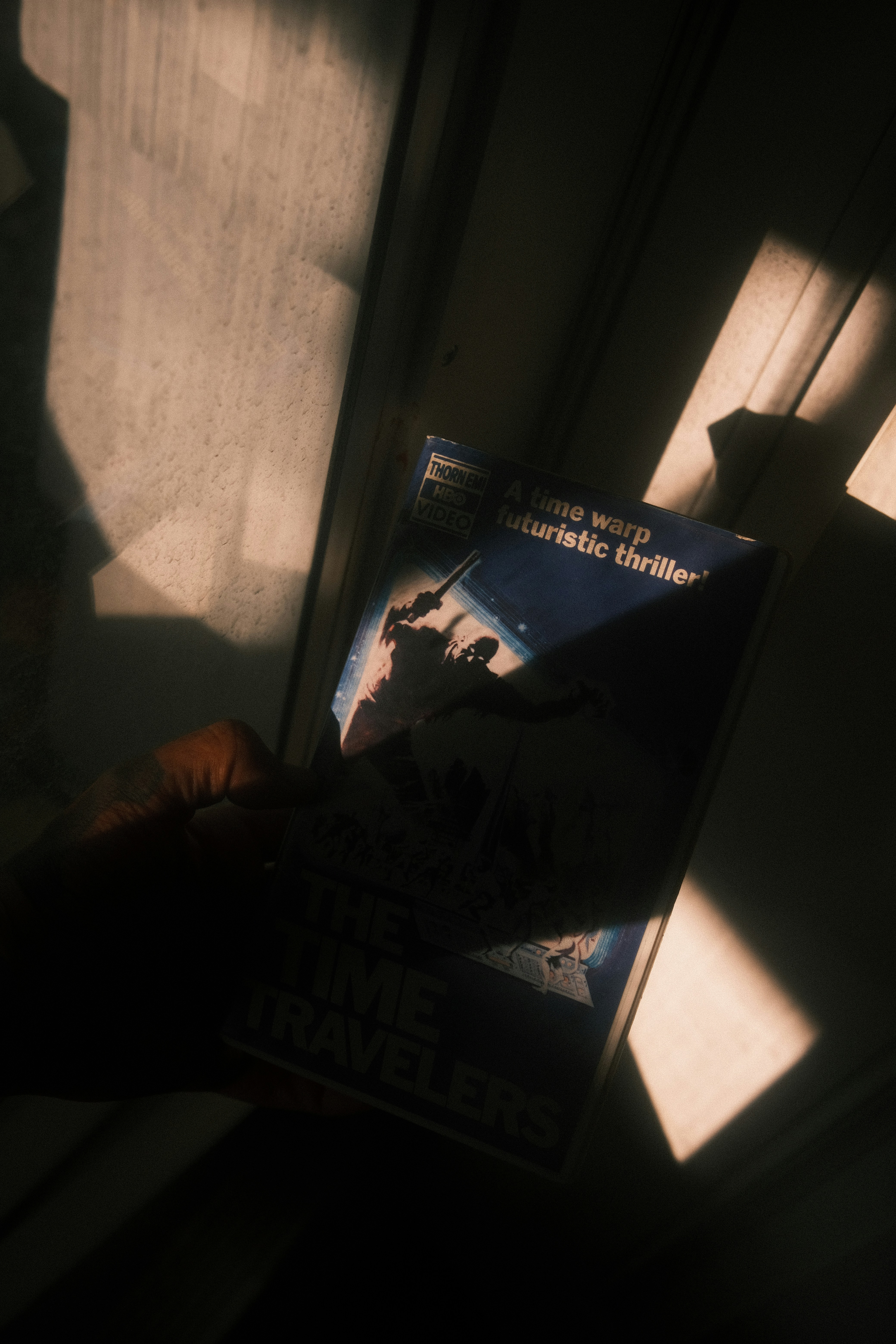 A hand holding "the time travelers" vhs tape in sunlight.