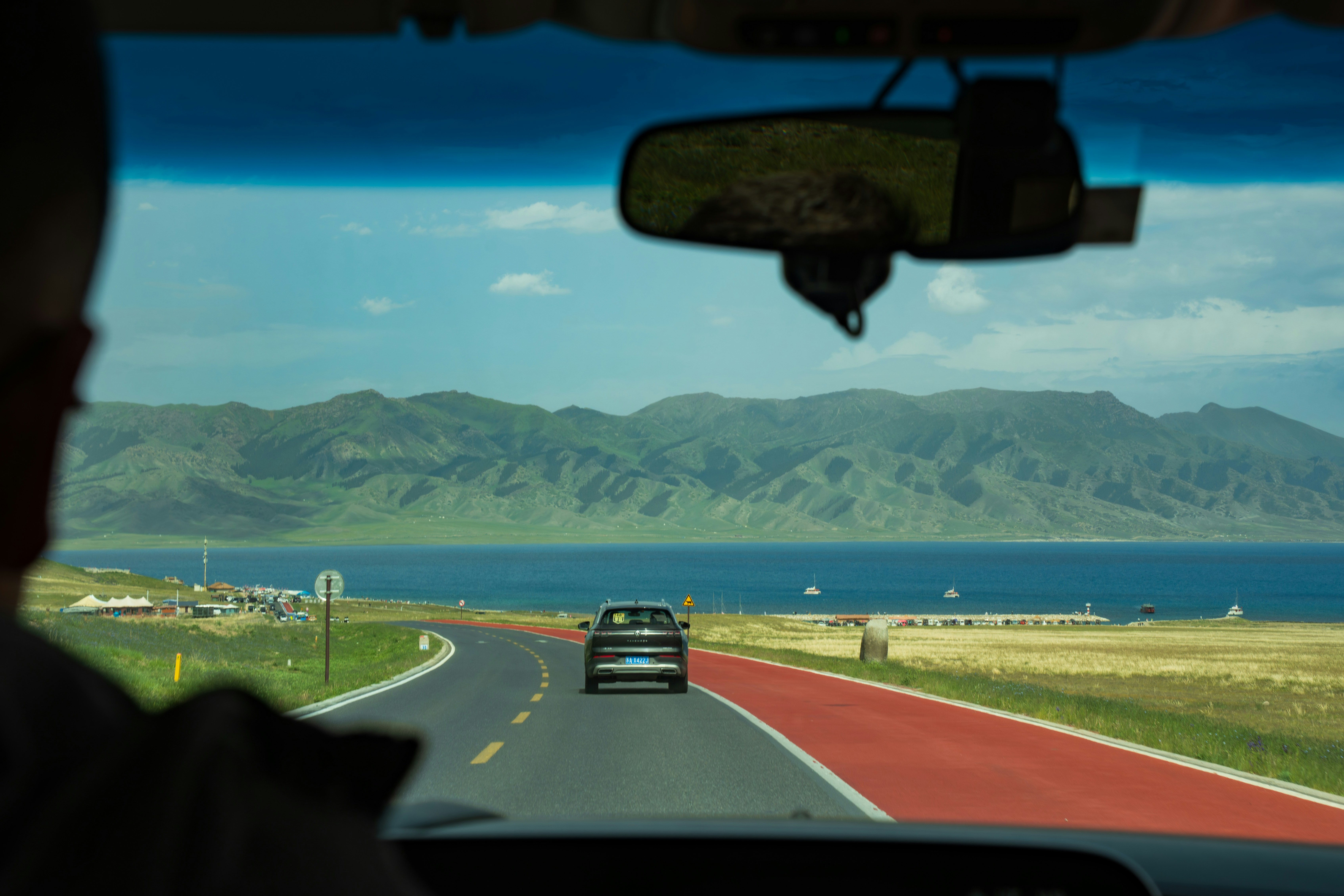 Driving on a scenic road beside a lake with mountains.