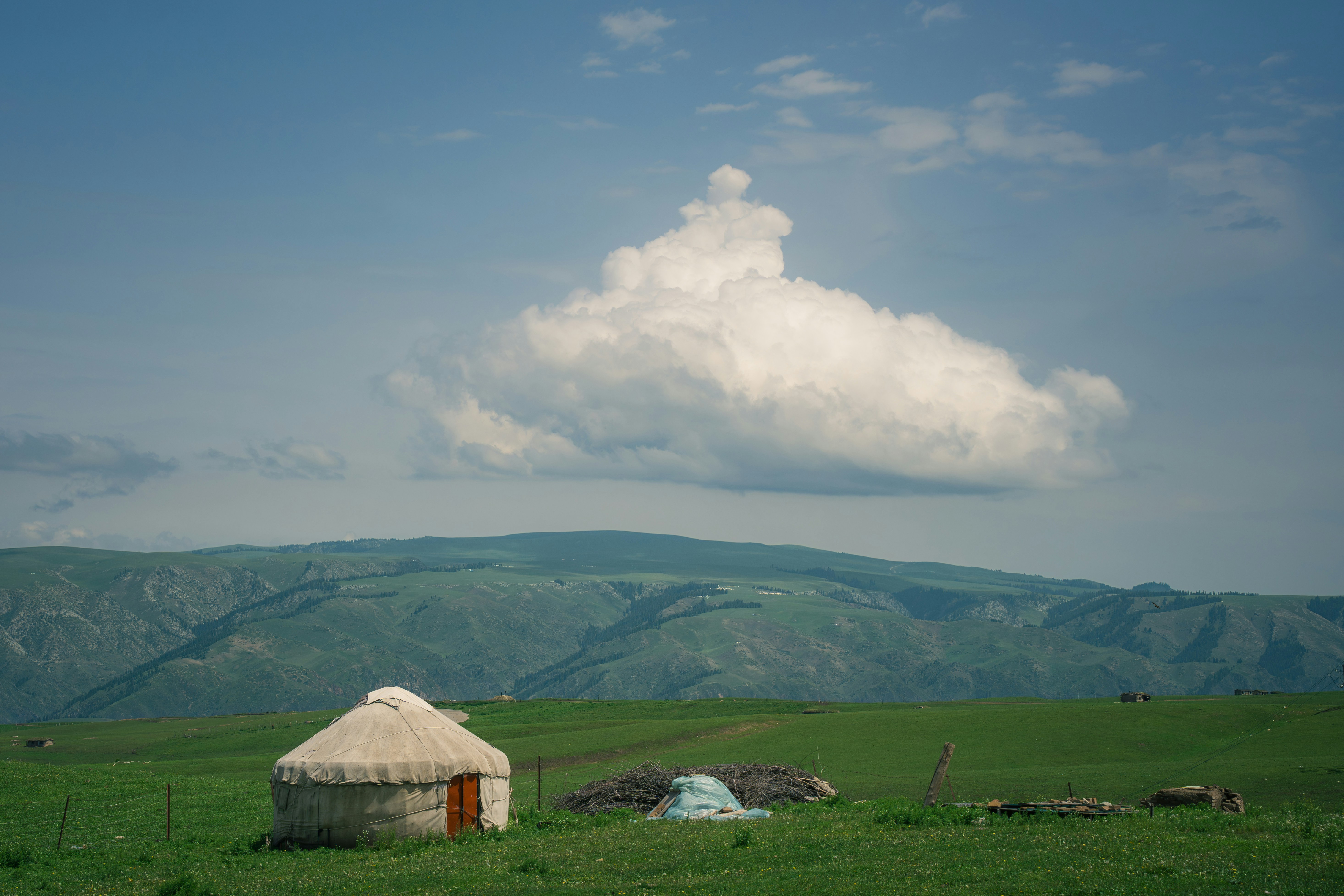 Yurt in a green field with mountains and a cloud.