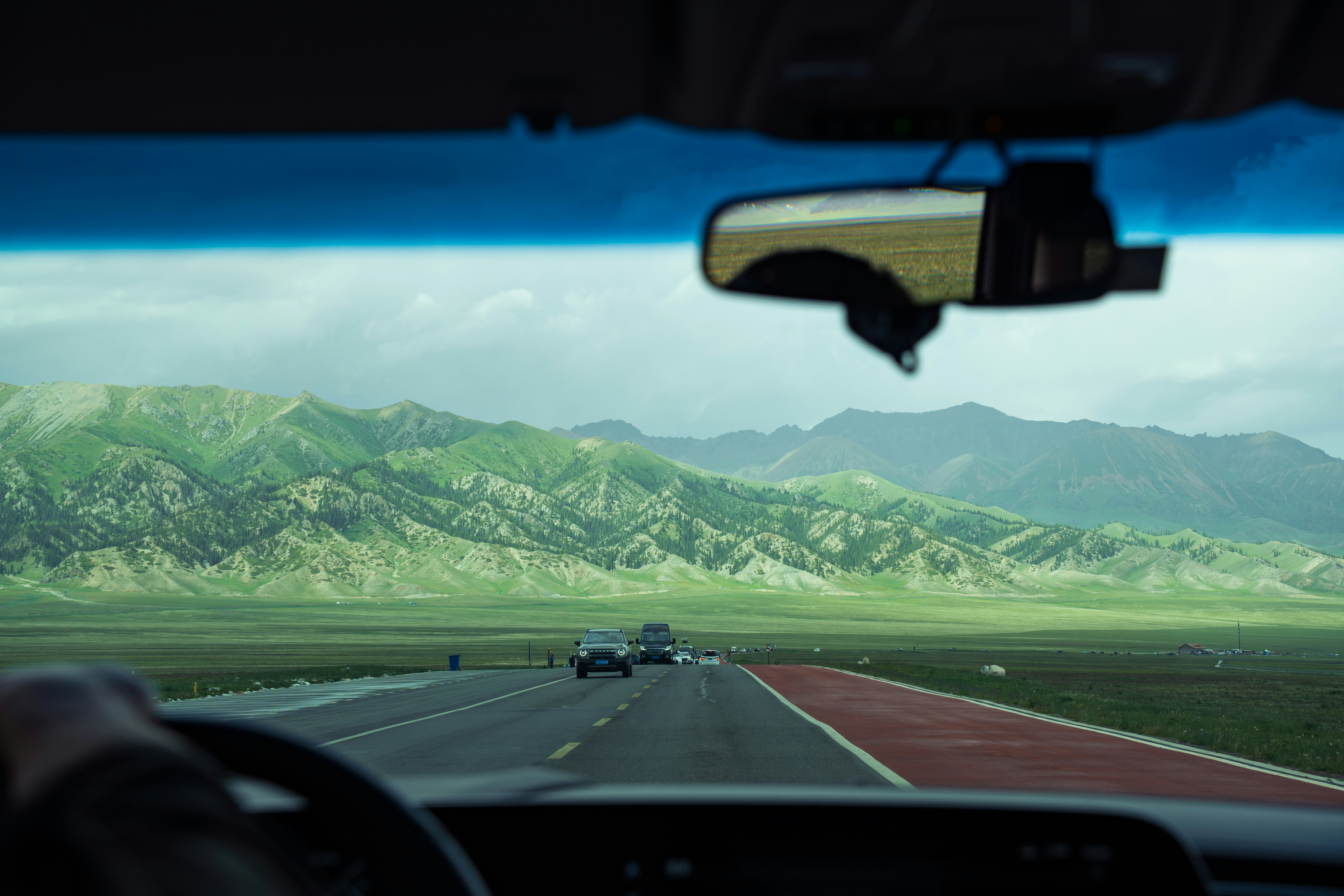 Driving on a highway through green mountains under cloudy sky.