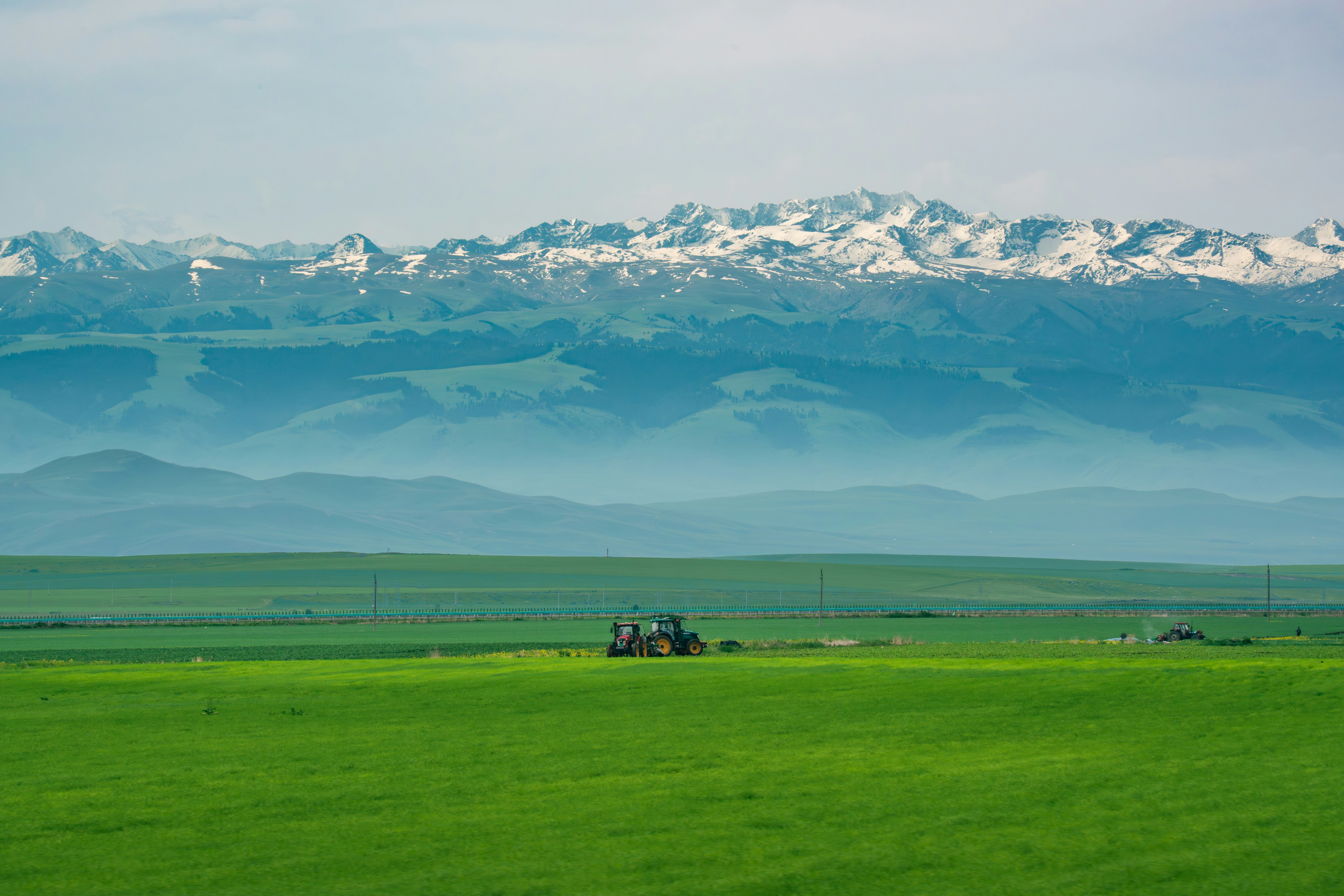 A tractor in a green field with snow-capped mountains.