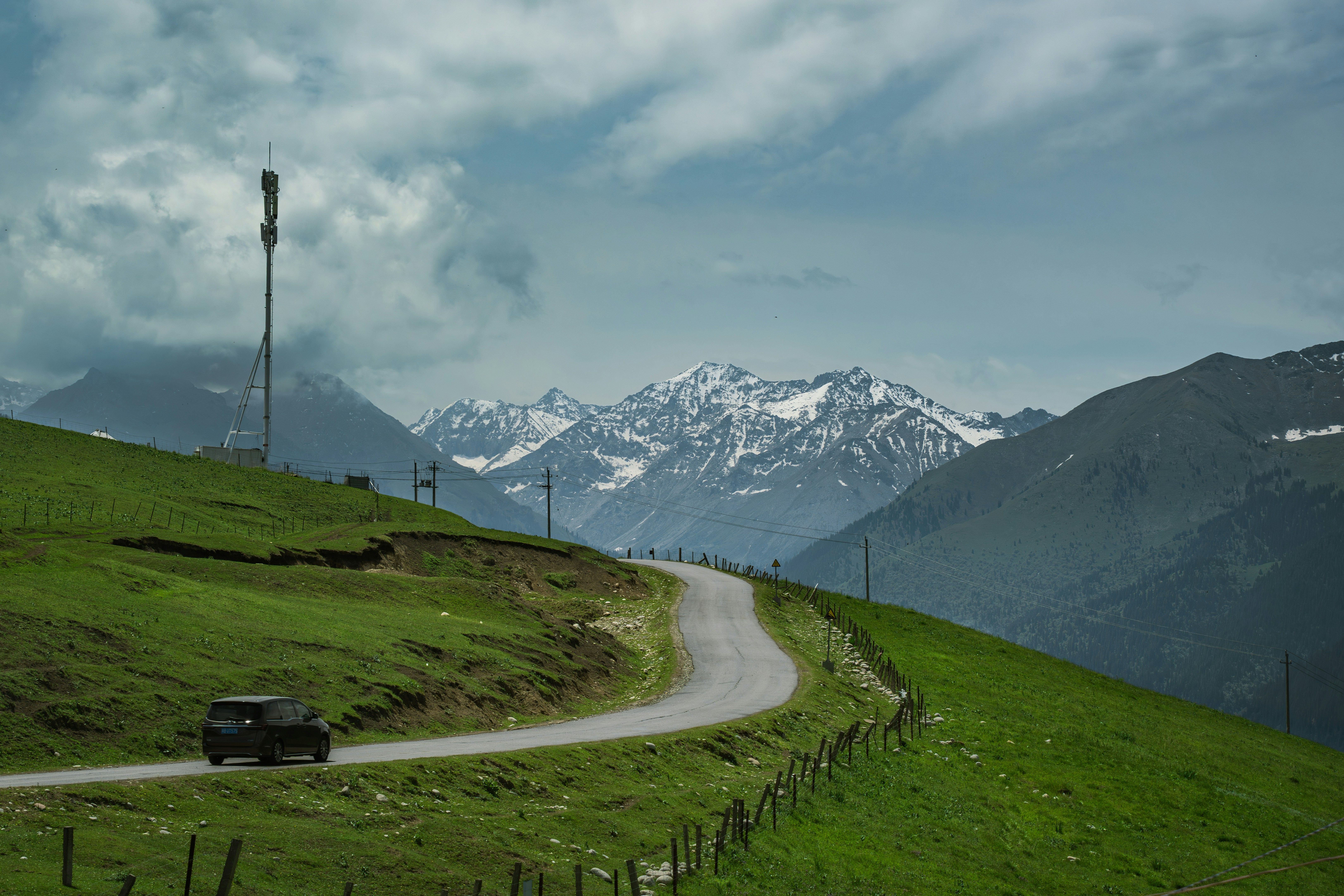 Car on a winding mountain road with snowy peaks.