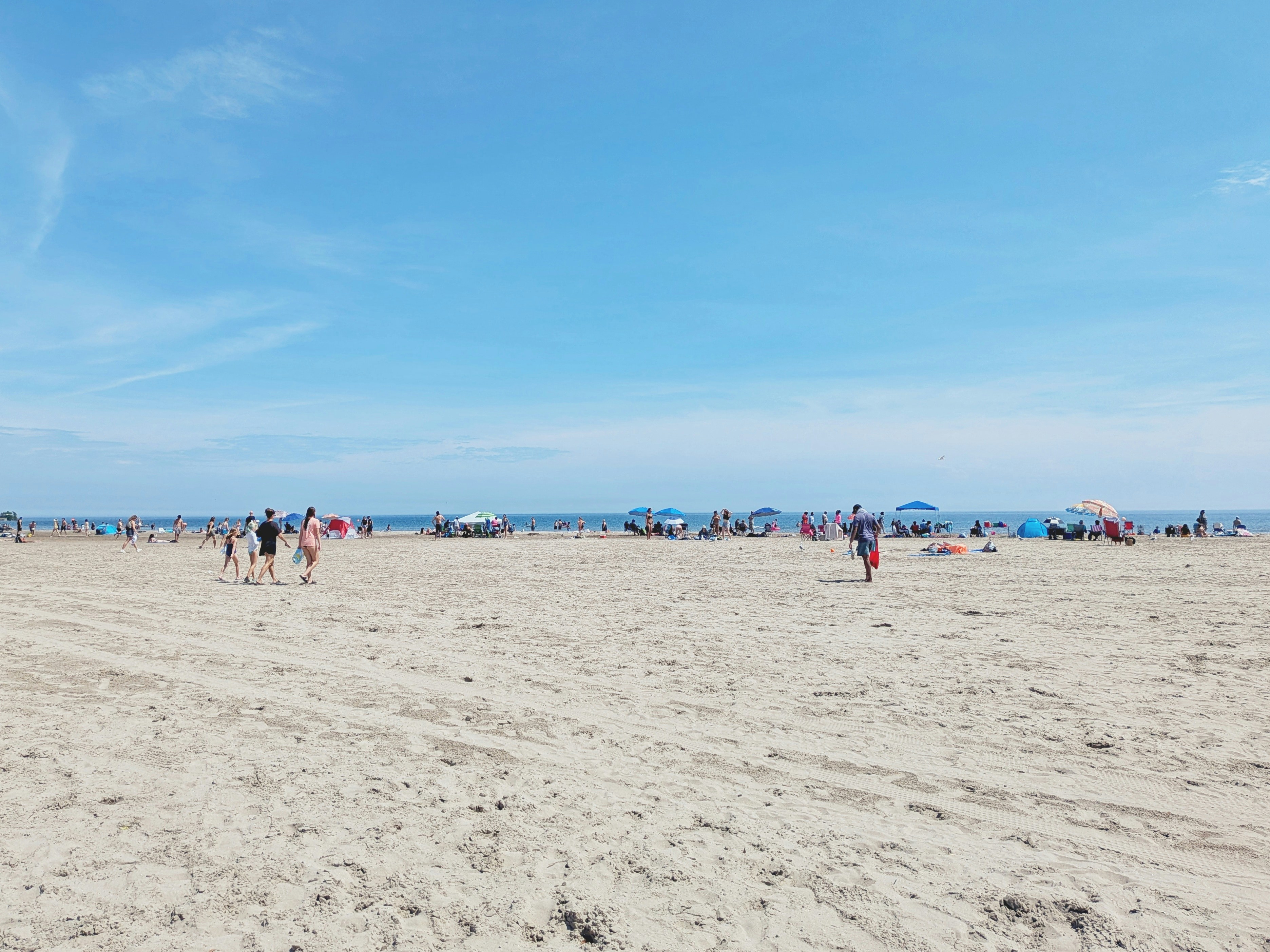 People enjoying a sunny day on a wide sandy beach.