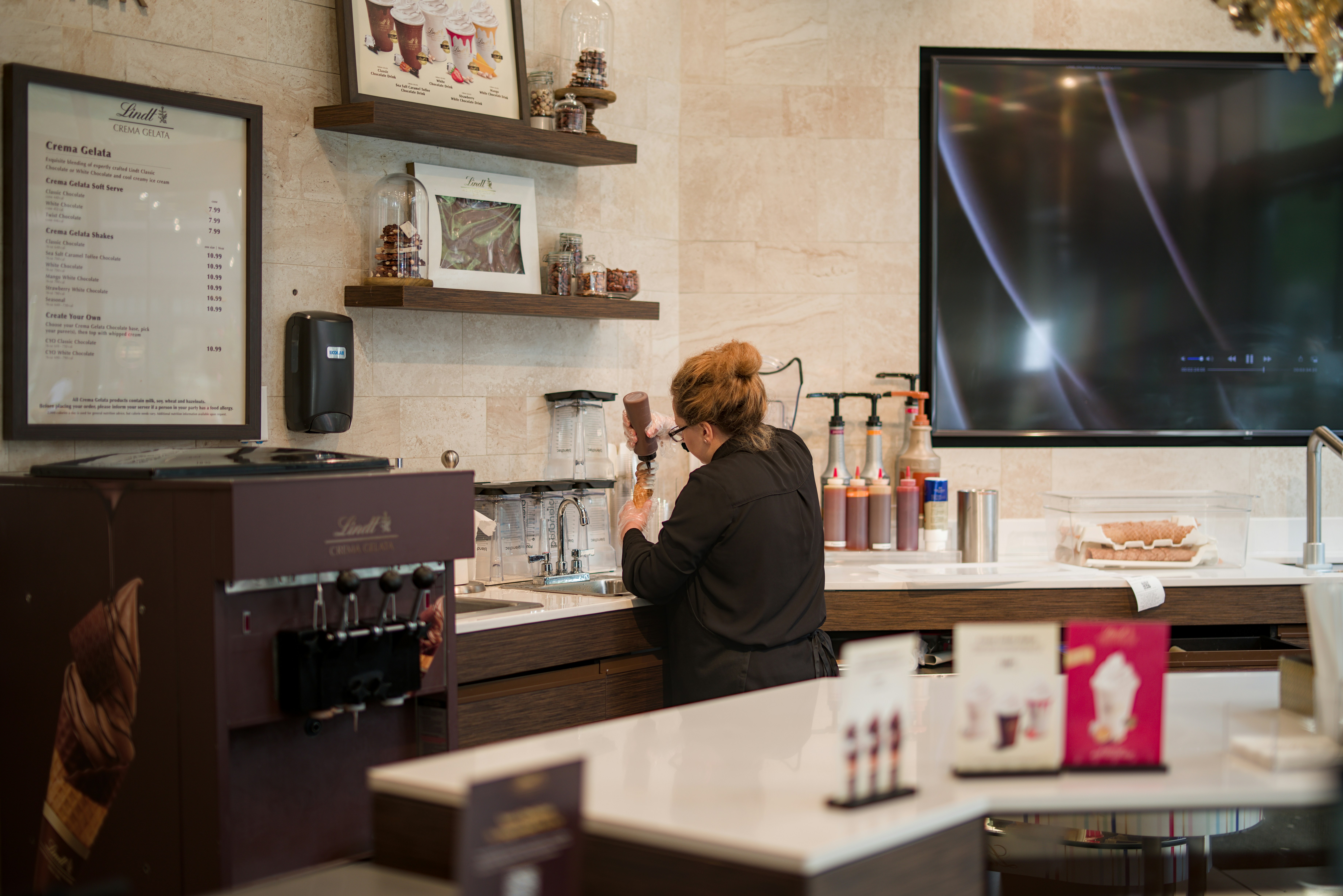 A cafe worker behind the counter where the ice bin and drinks station sit