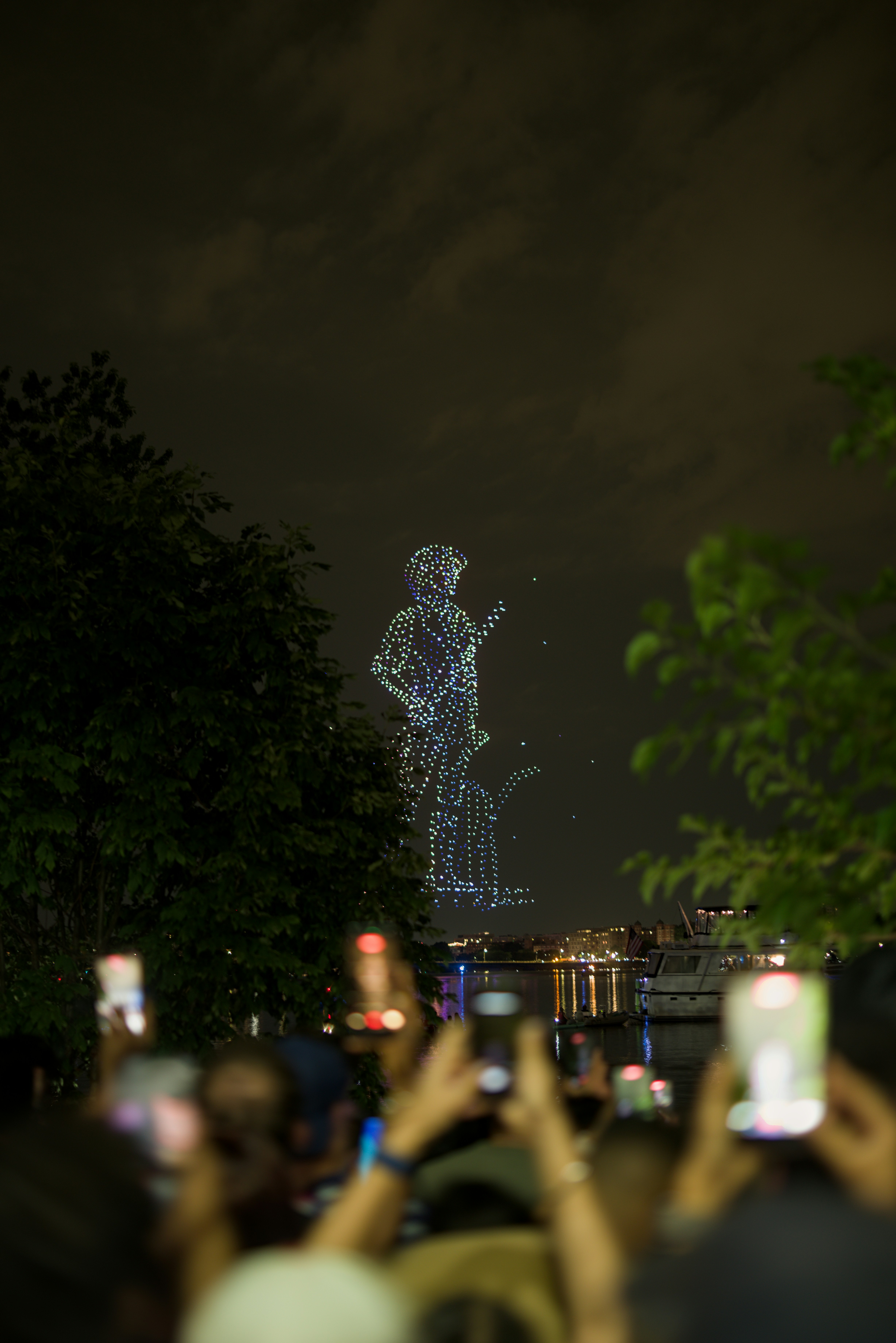 Drone light show forms guitarist in night sky above crowd.