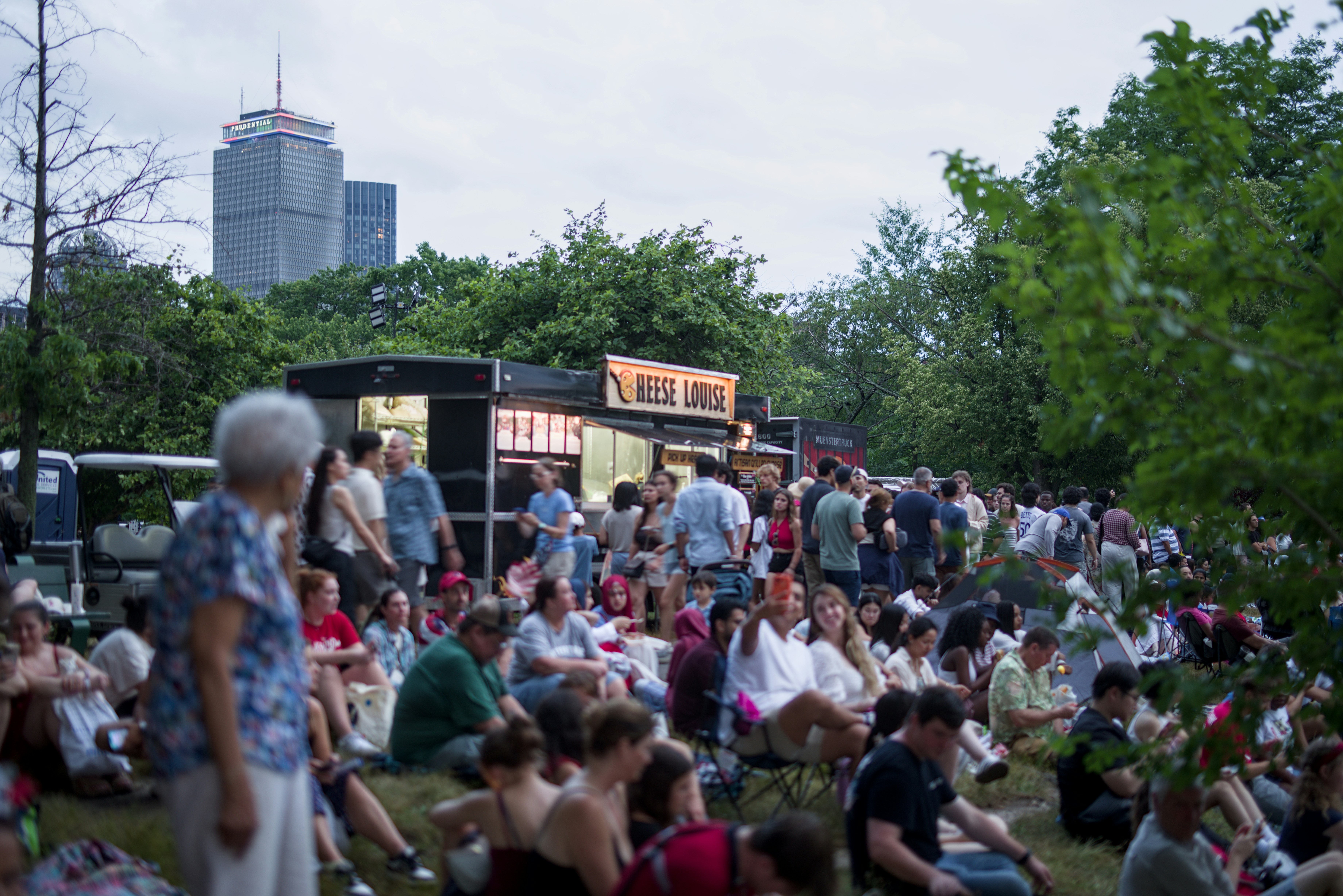 청춘컴퍼니 - Crowd gathered on grass near food trucks with city skyline