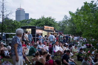 Crowd gathered on grass near food trucks with city skyline.