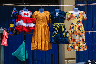 Colorful dresses on mannequins and hangers against a blue wall.