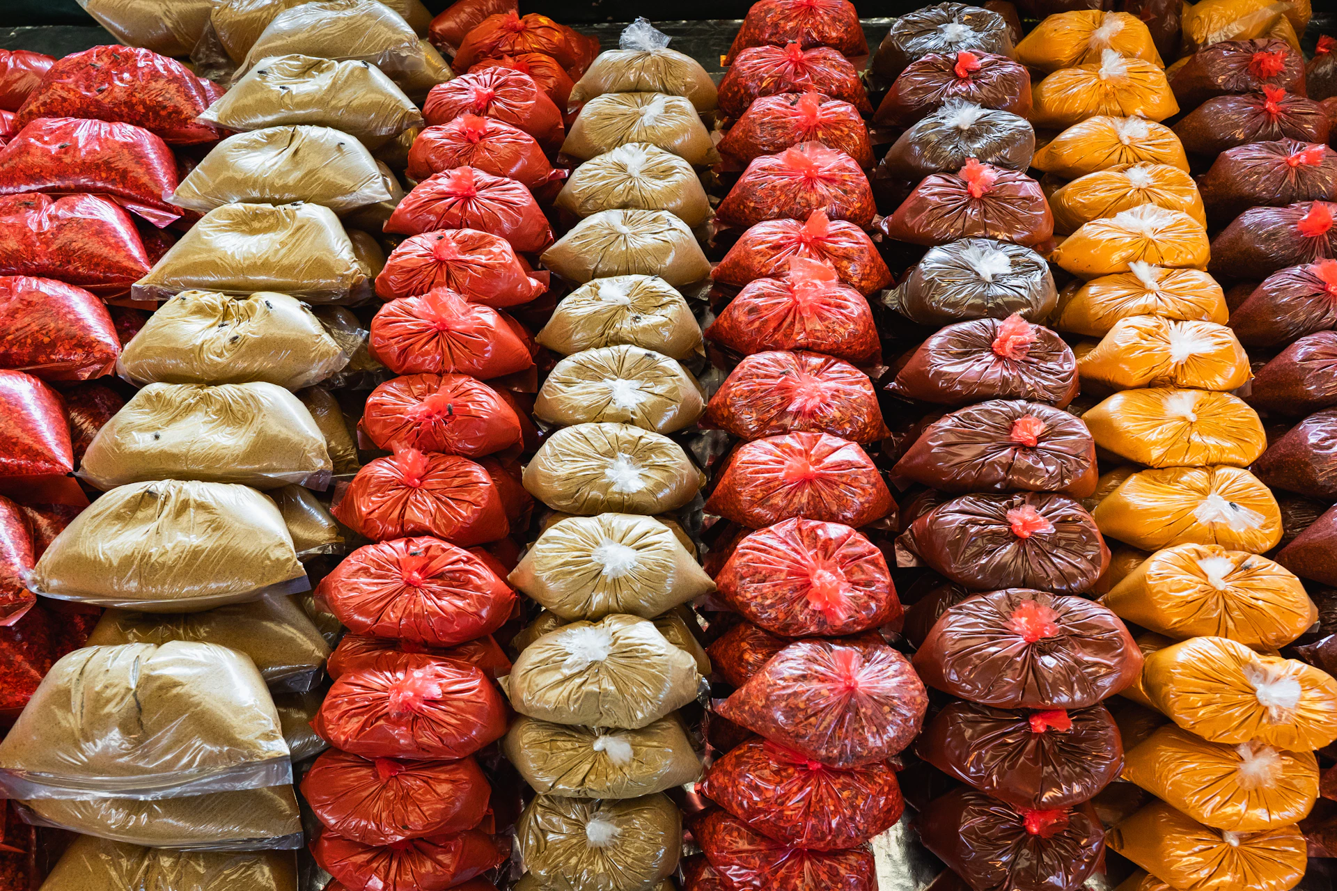 Rows of colorful spices in plastic bags at a market.