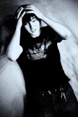 Young person with hands on head, wearing dark clothing.