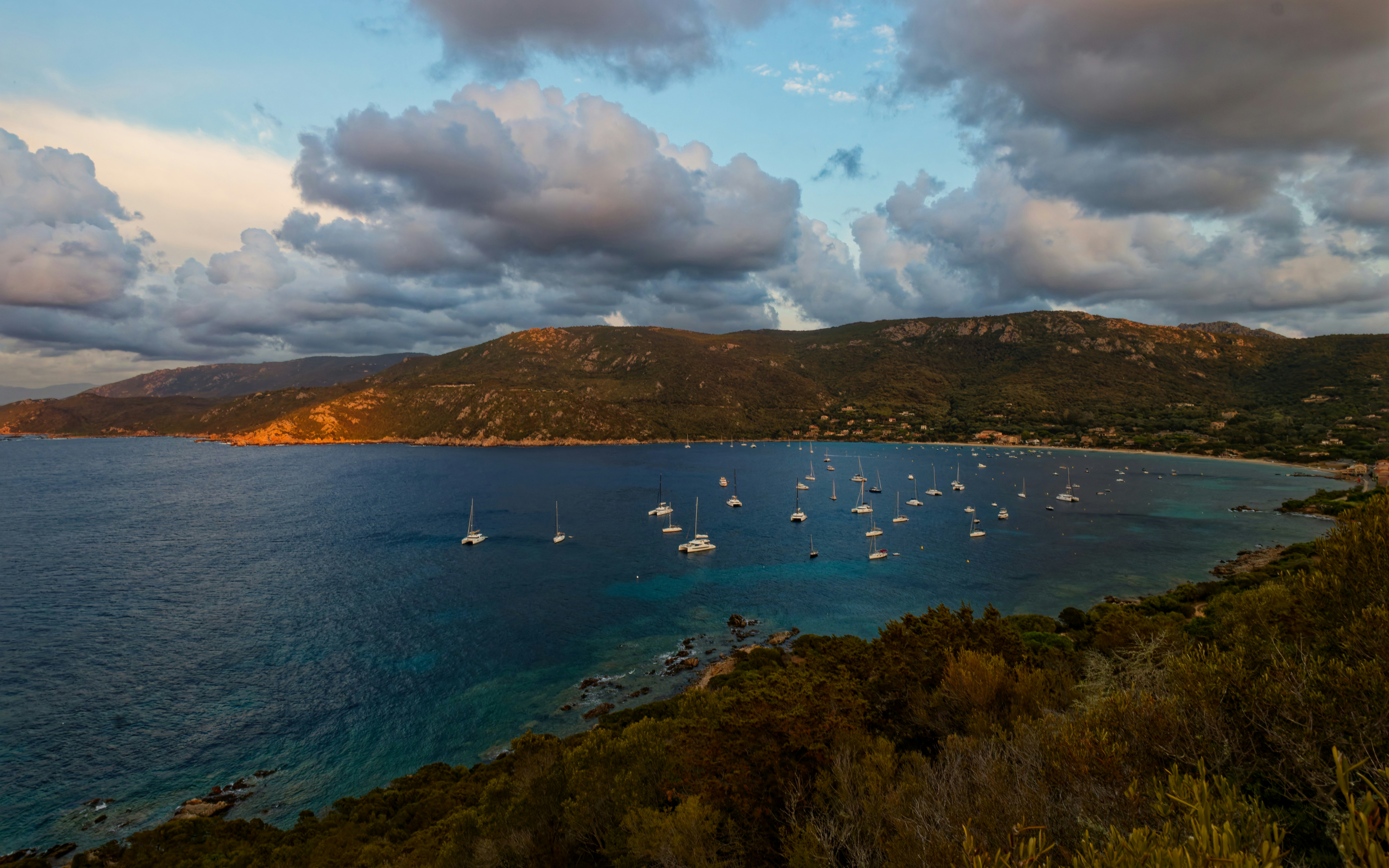 Boats in a bay with mountains under a cloudy sunset