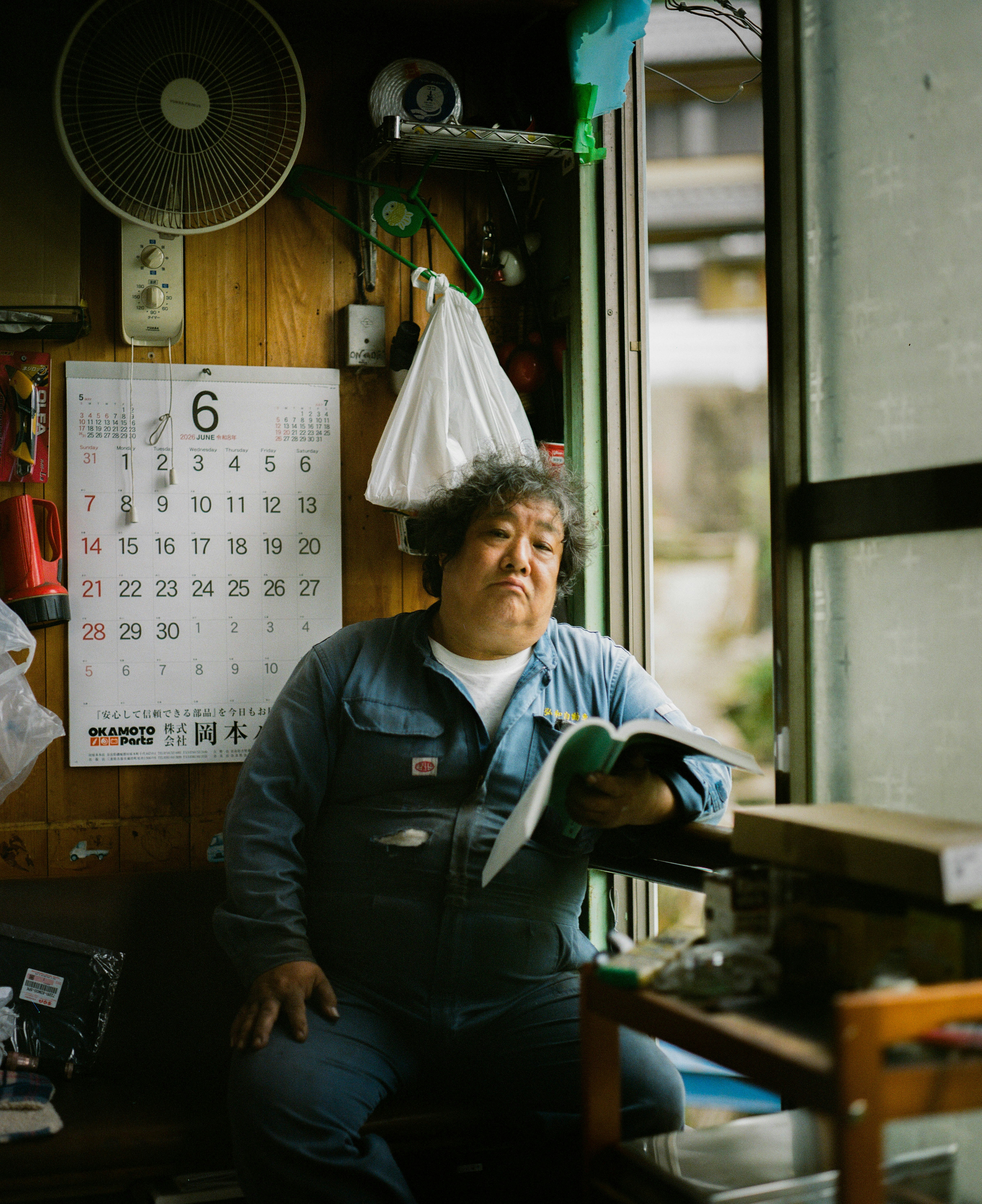 Pensive man in blue overalls holding a book indoors.