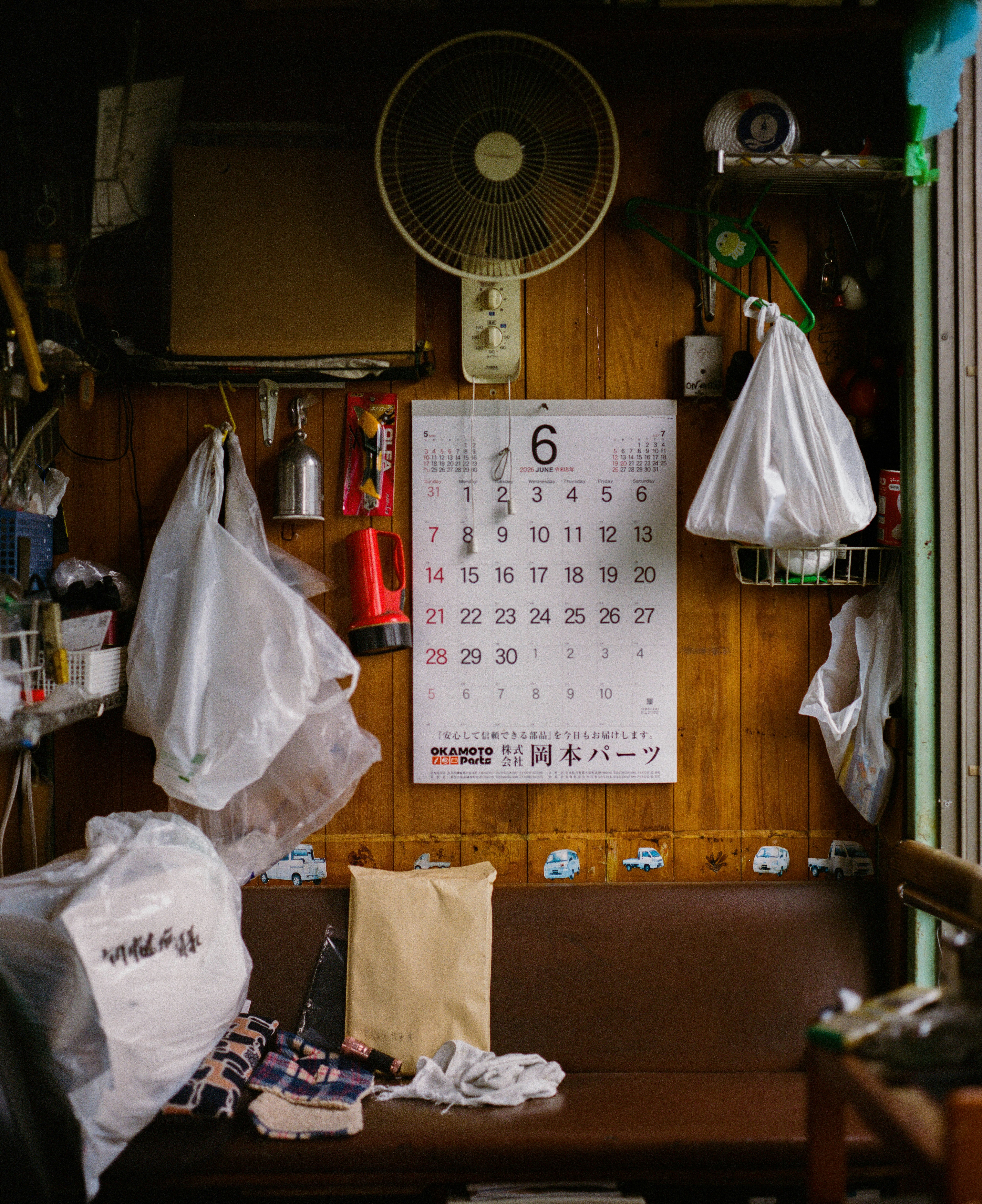 Cluttered wooden wall with a calendar, fan, and hanging bags