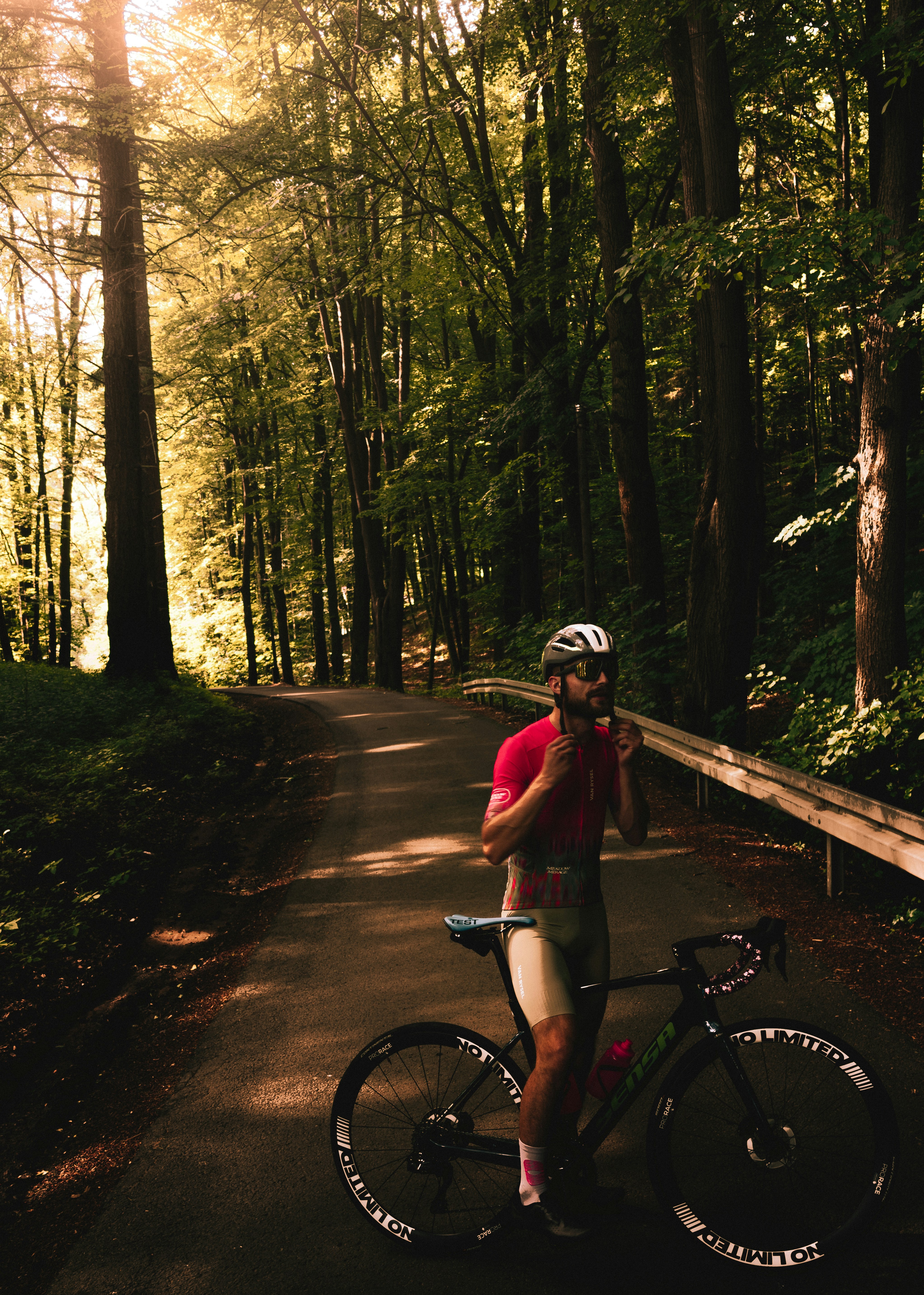 Cyclist standing with bike on a sunlit forest path.