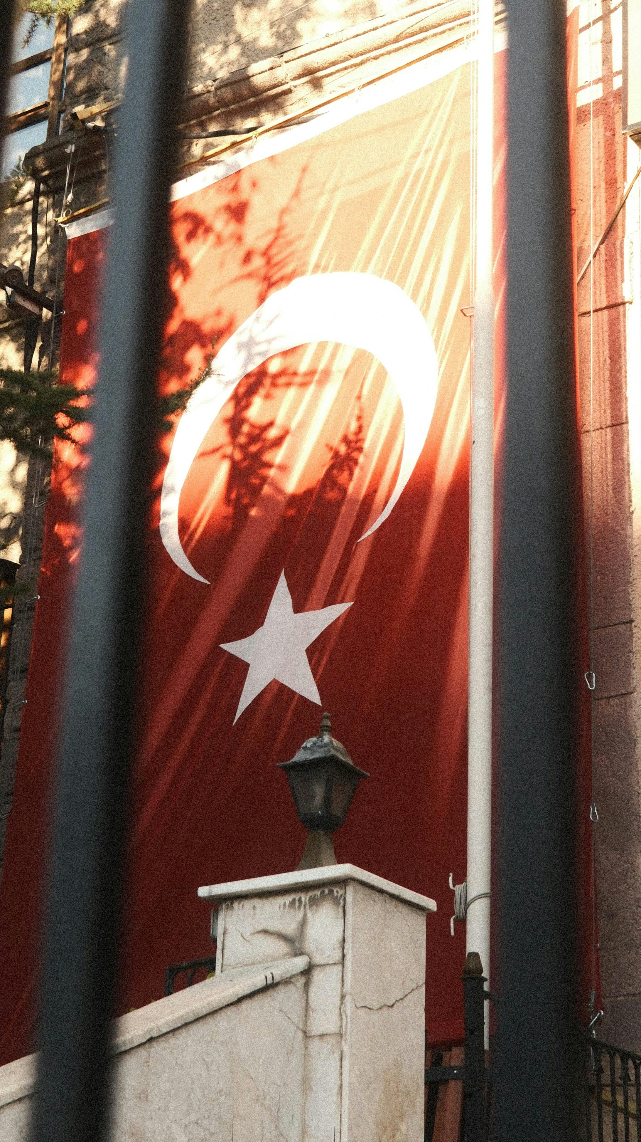 Sunlight illuminates the turkish flag behind a metal fence
