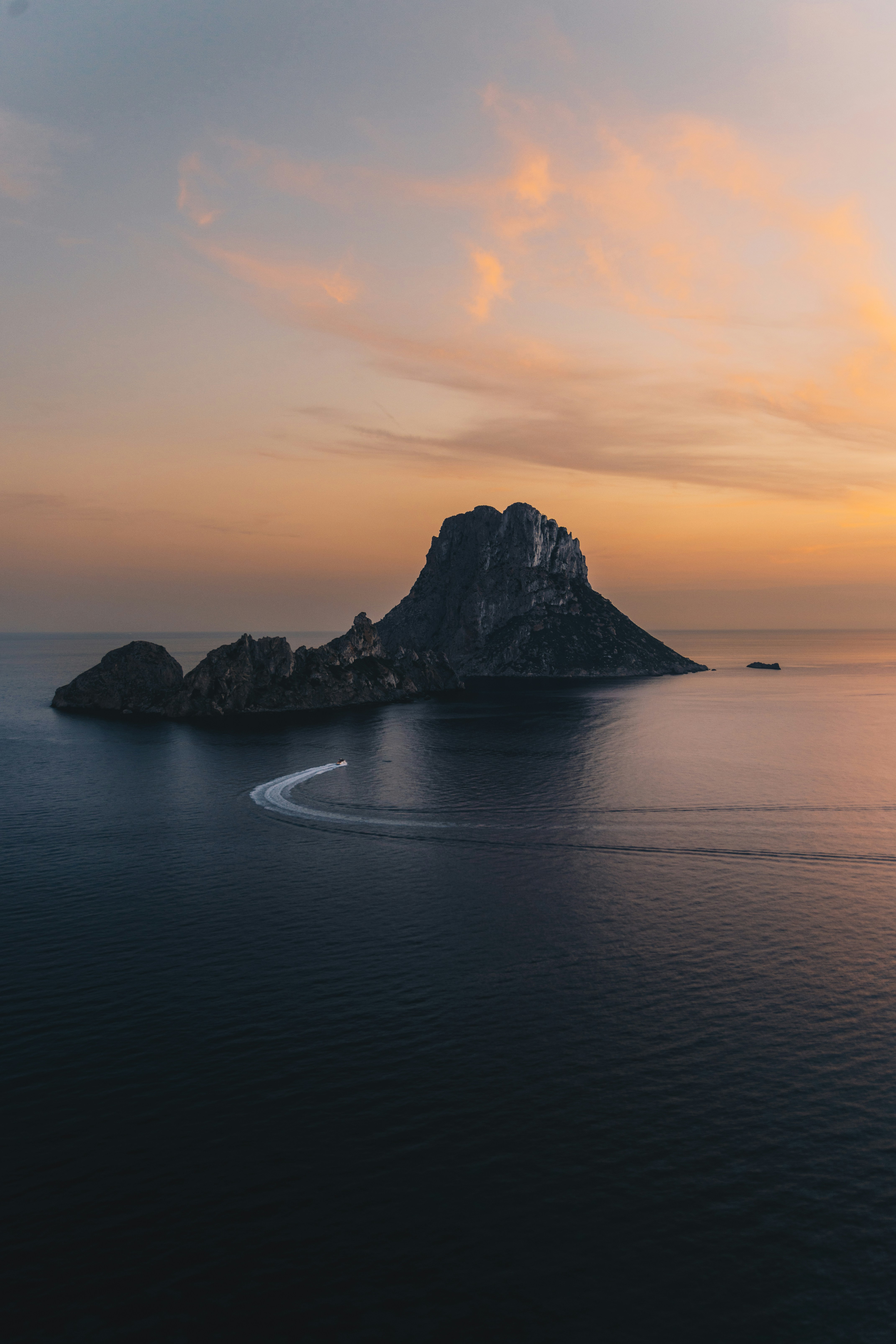 A boat speeds past a rocky island at sunset.
