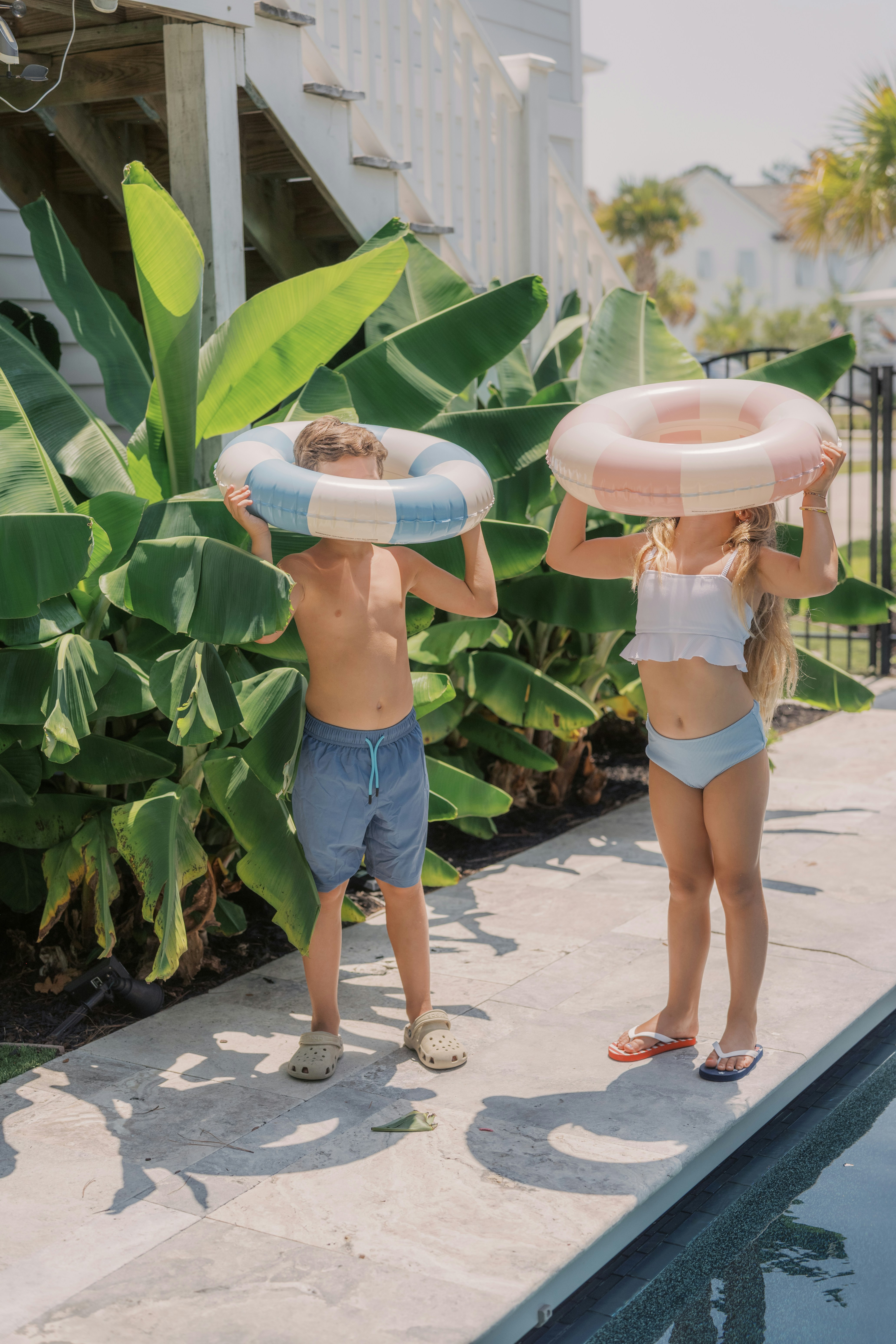 Children with swim rings standing by a tropical pool.