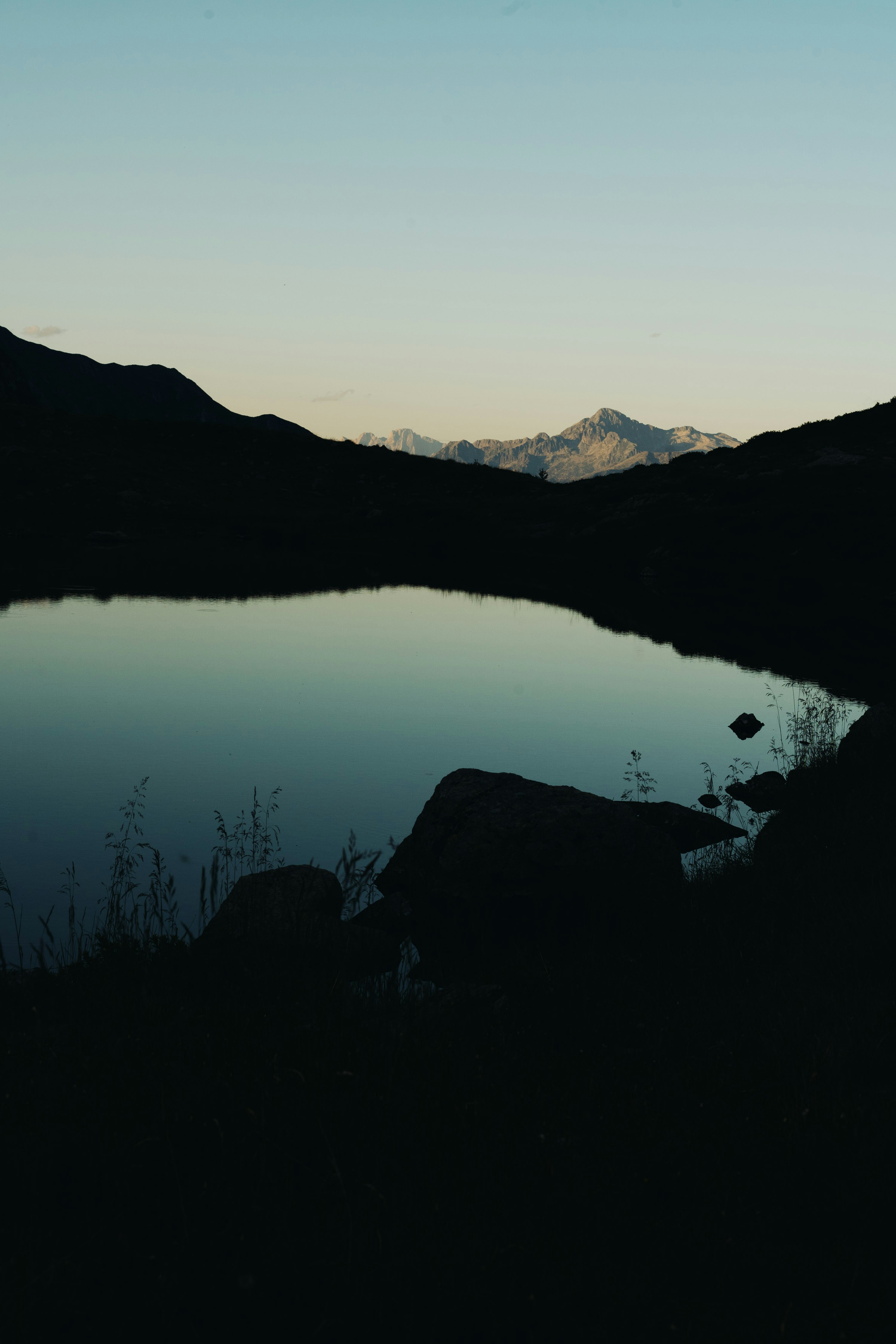 Tranquil mountain lake at dawn with distant snow-capped peaks.
