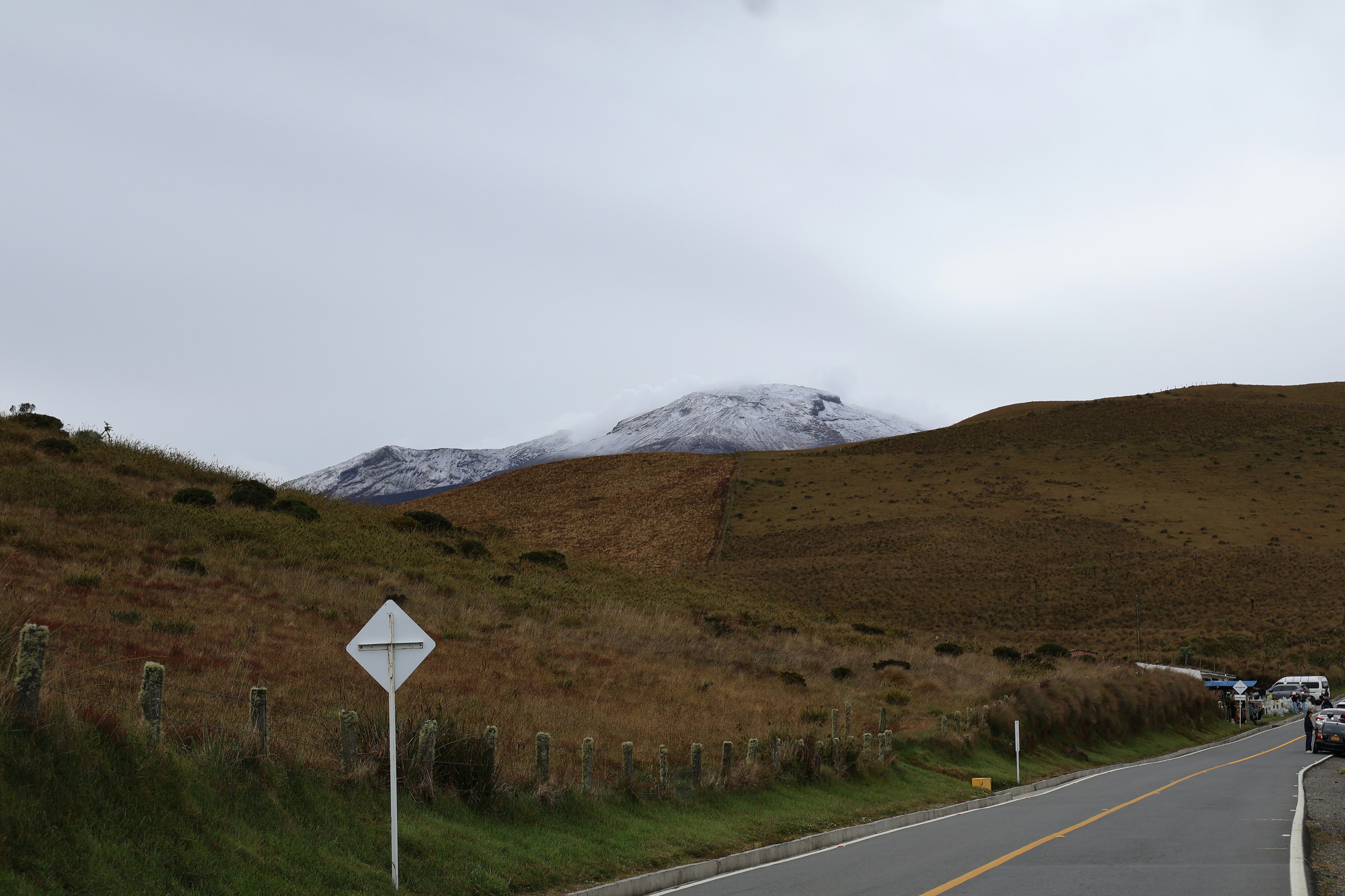 A road winds through brown hills towards a snow-capped mountain.