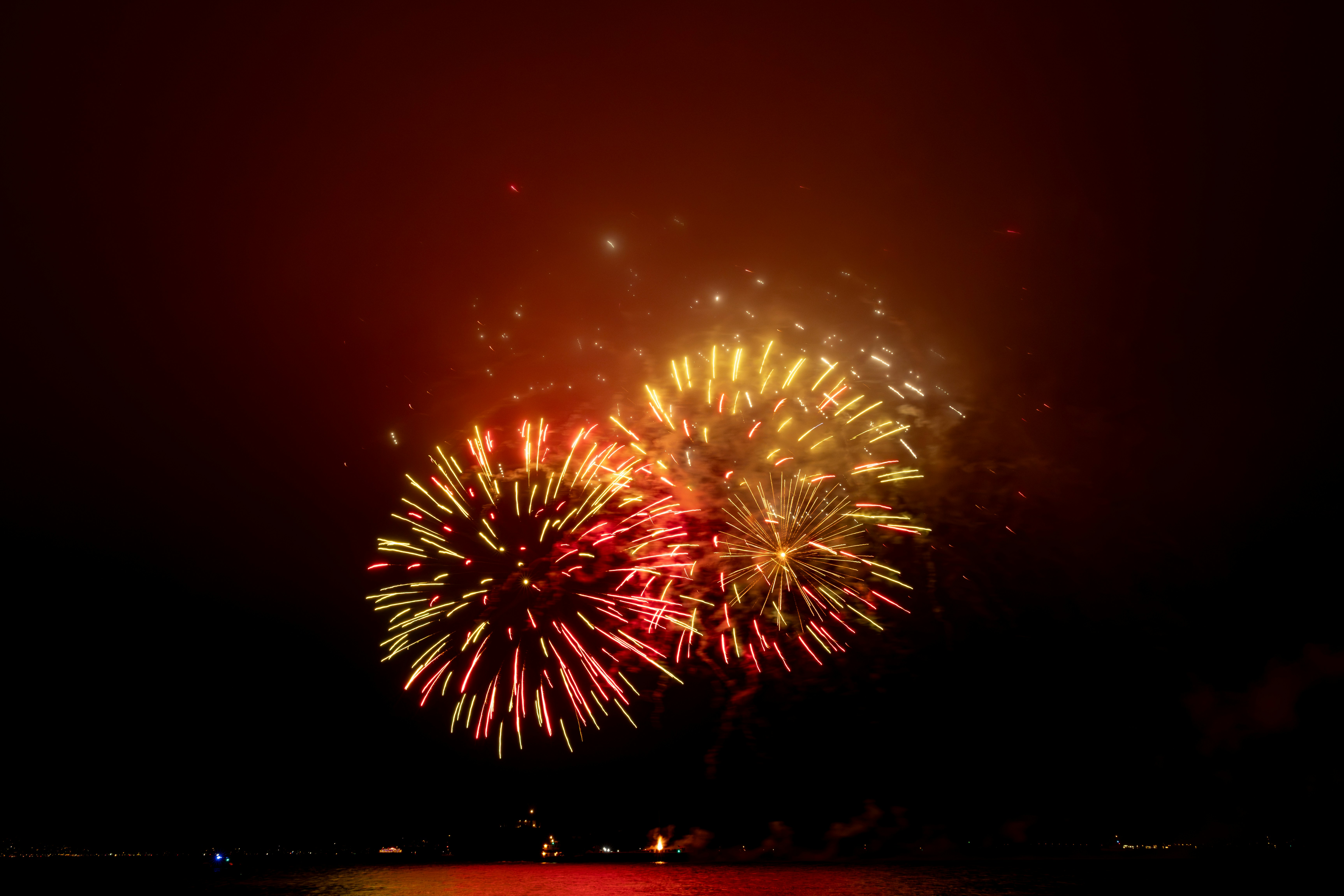 Colorful fireworks explode over dark water at night.