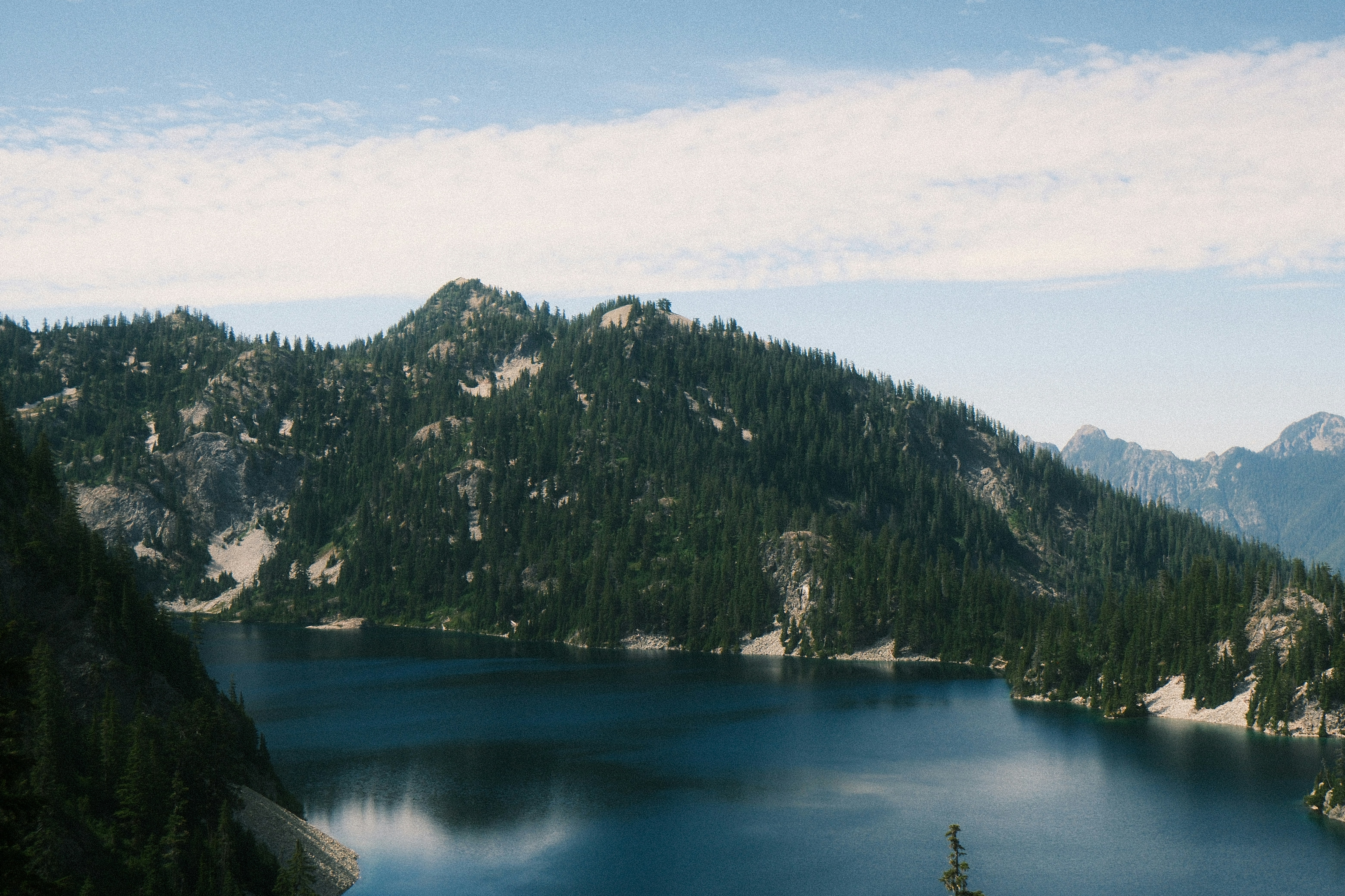 Serene blue lake surrounded by forested mountains and snow.