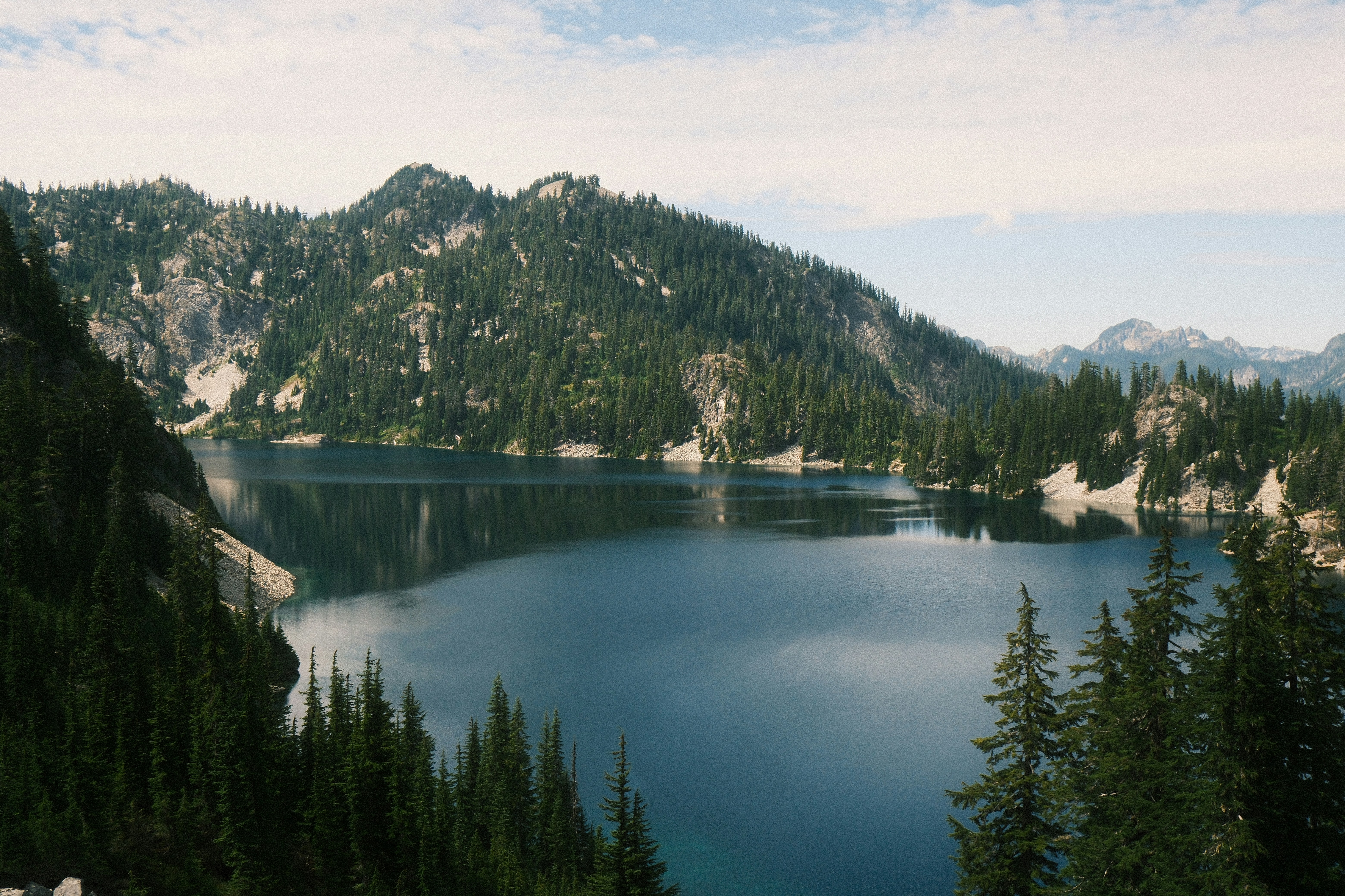 Scenic lake nestled among forested mountains and distant peaks.