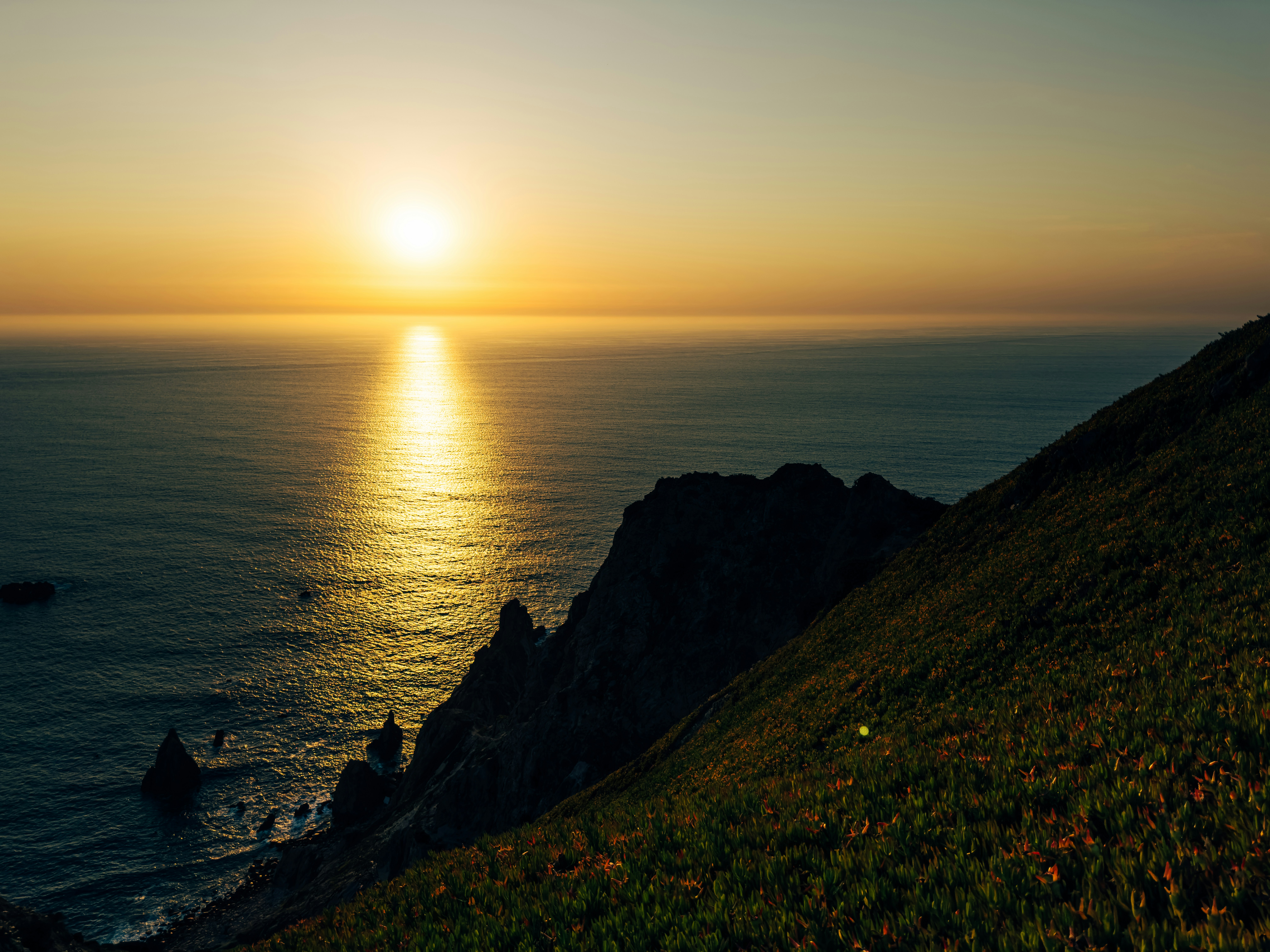 海の上に輝く鮮やかな夕焼けと、急な緑の崖。