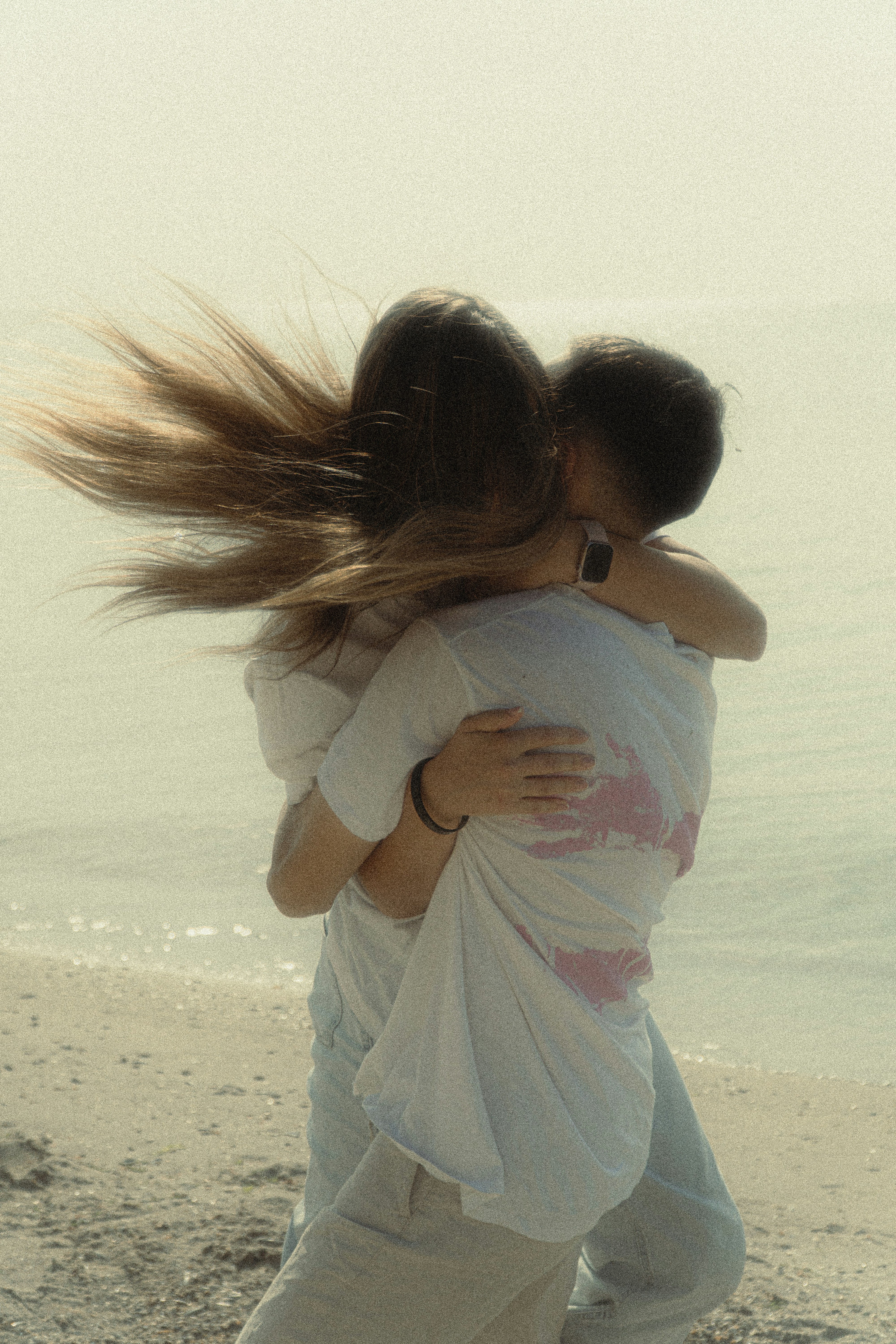 Two people hugging on a sandy beach with windblown hair.