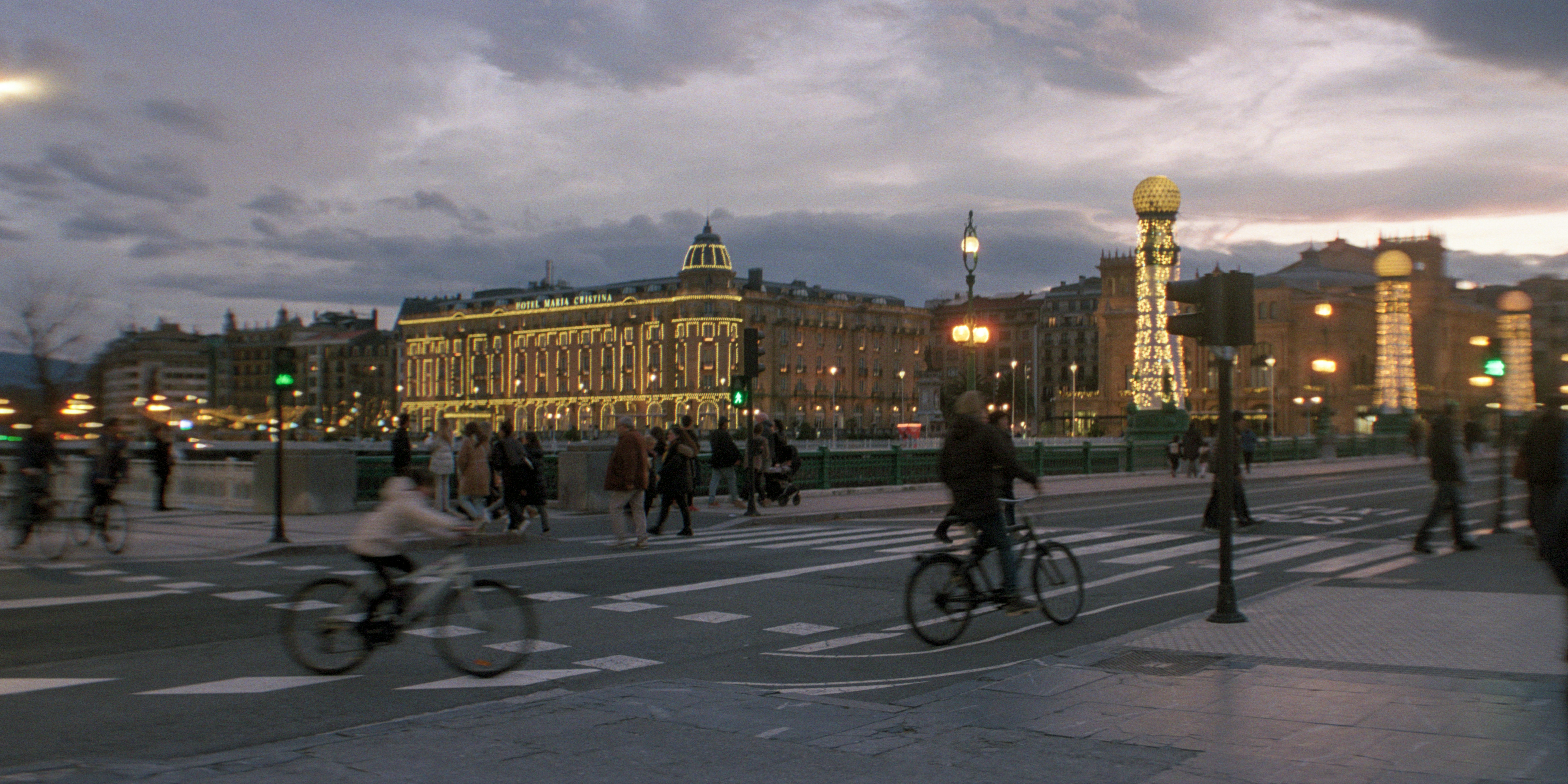 Evening city scene with pedestrians, cyclists, and illuminated buildings.