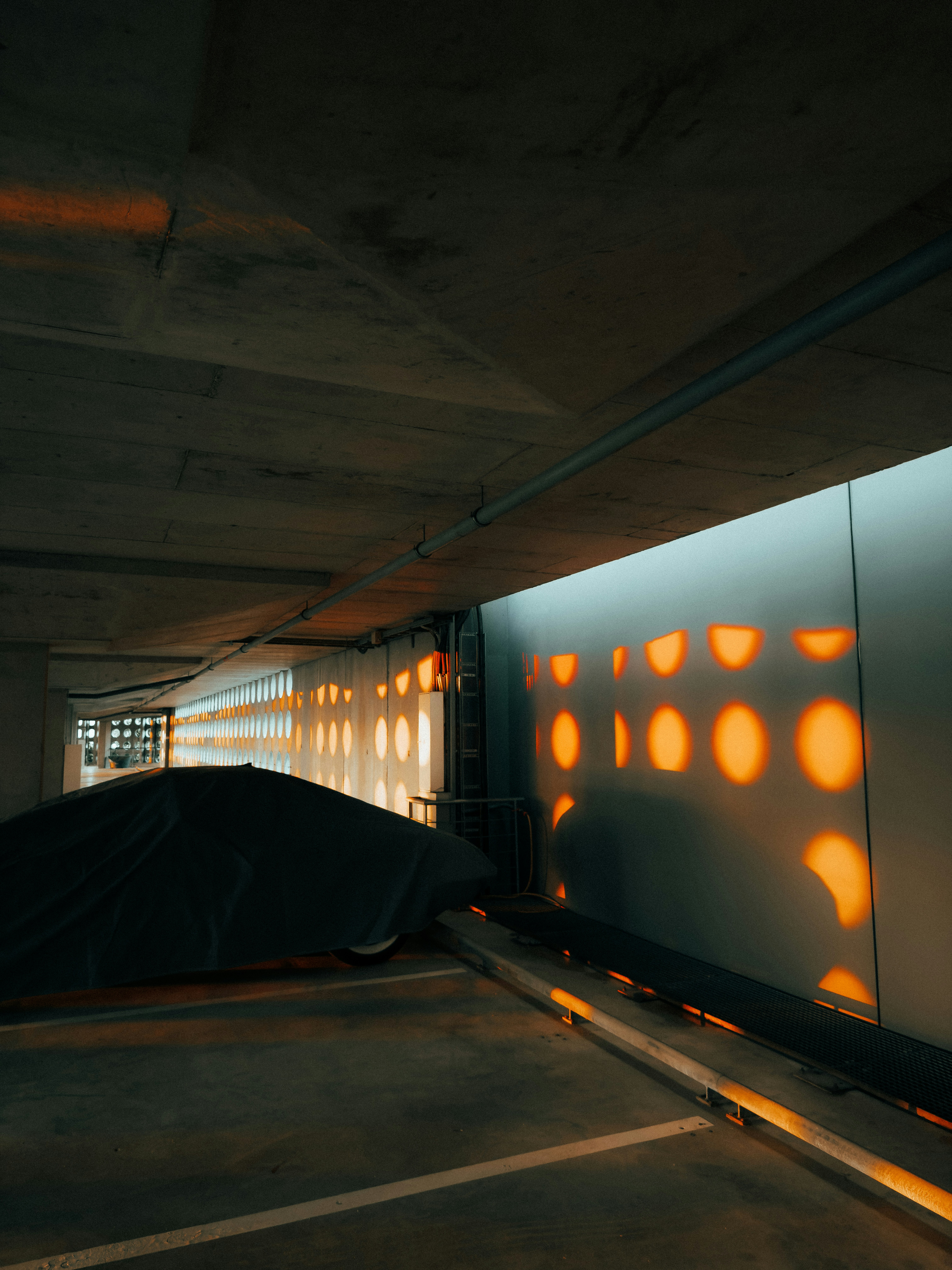 Des motifs lumineux orange illuminent un parking en béton sombre.