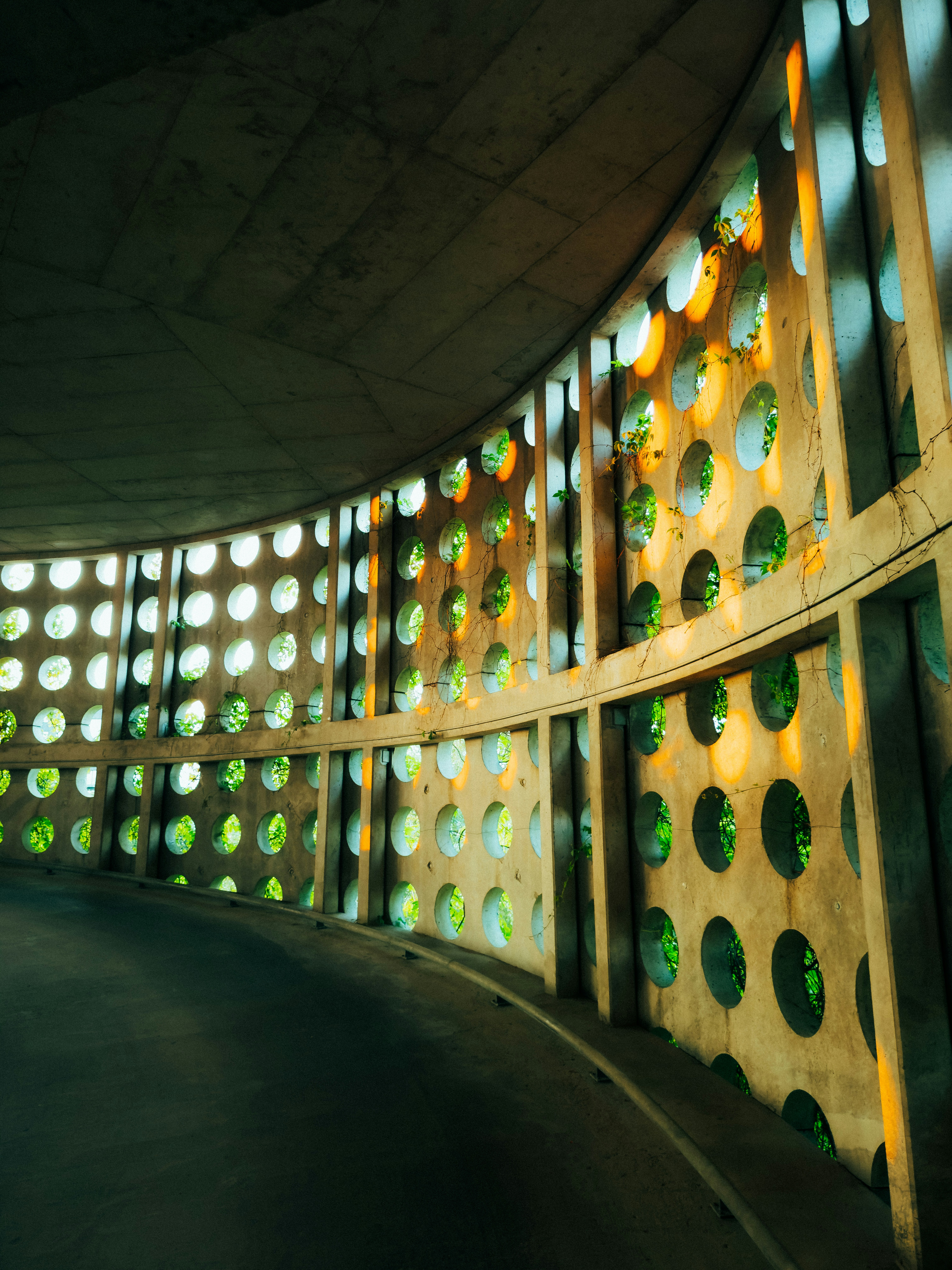 La lumière du soleil filtre à travers des ouvertures circulaires dans un mur de béton courbé.