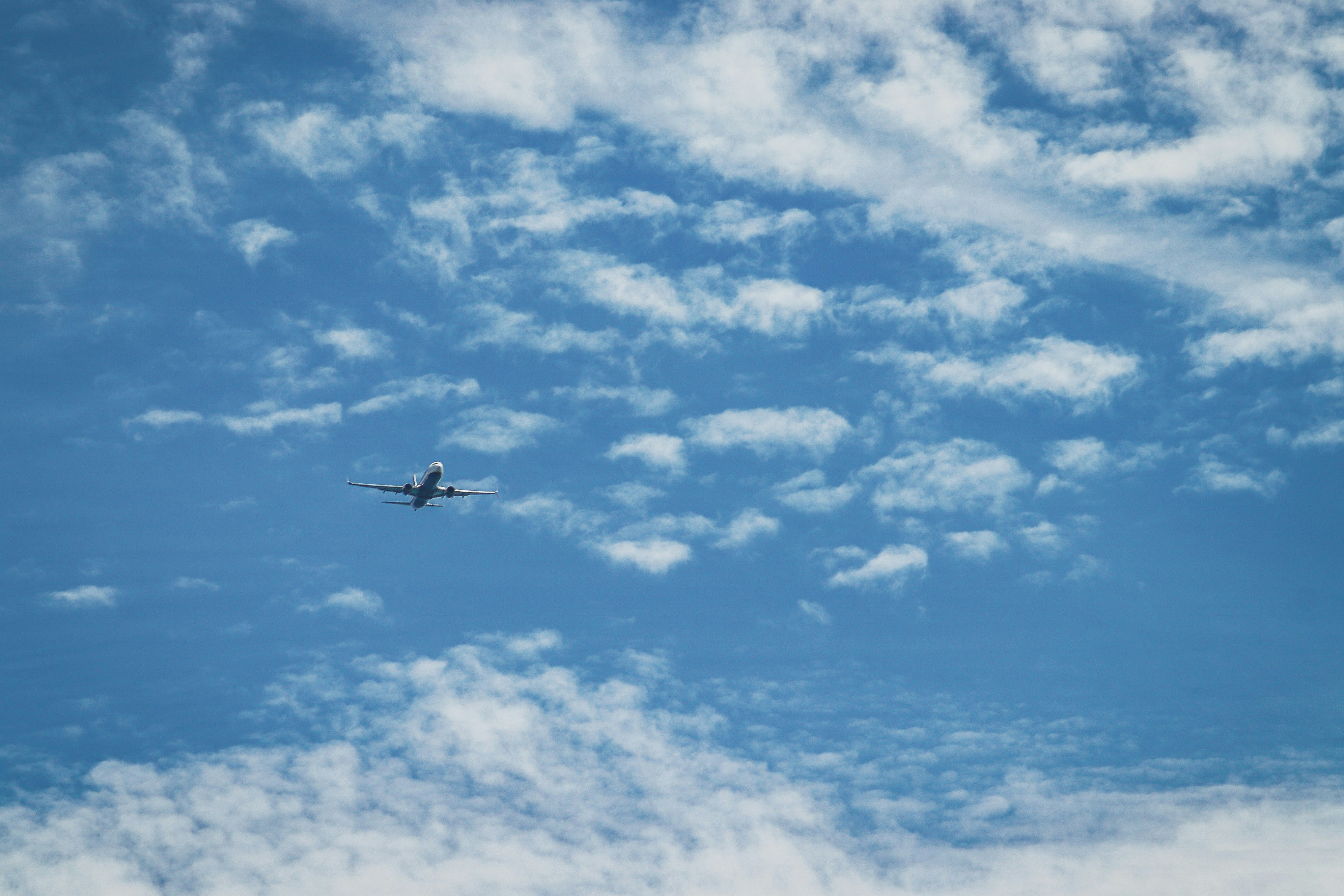 Airplane flying in a blue sky with white clouds.