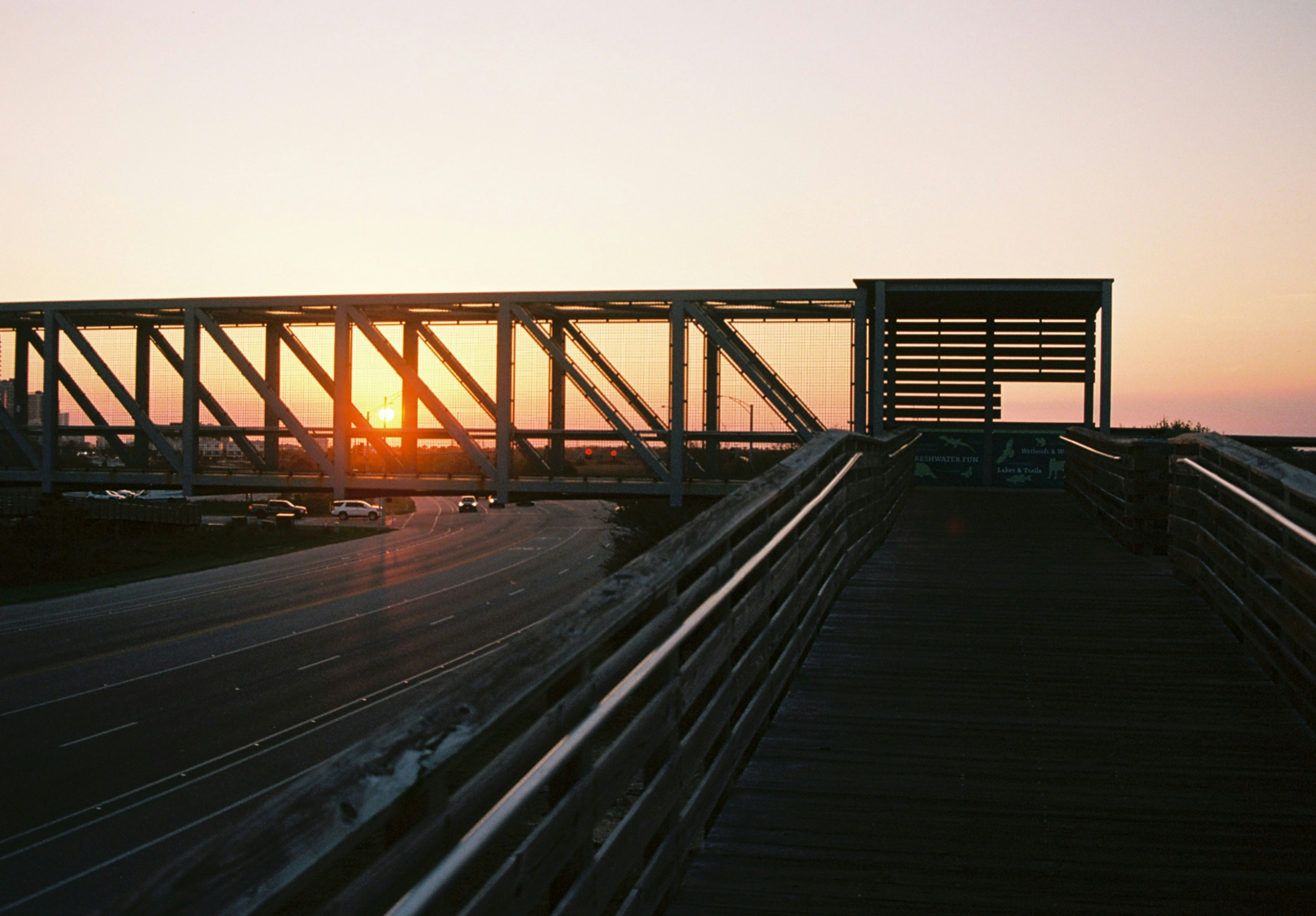 A pedestrian bridge crosses over a road at sunset.