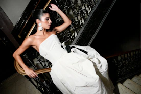 Woman in white strapless dress posing on a dark staircase.