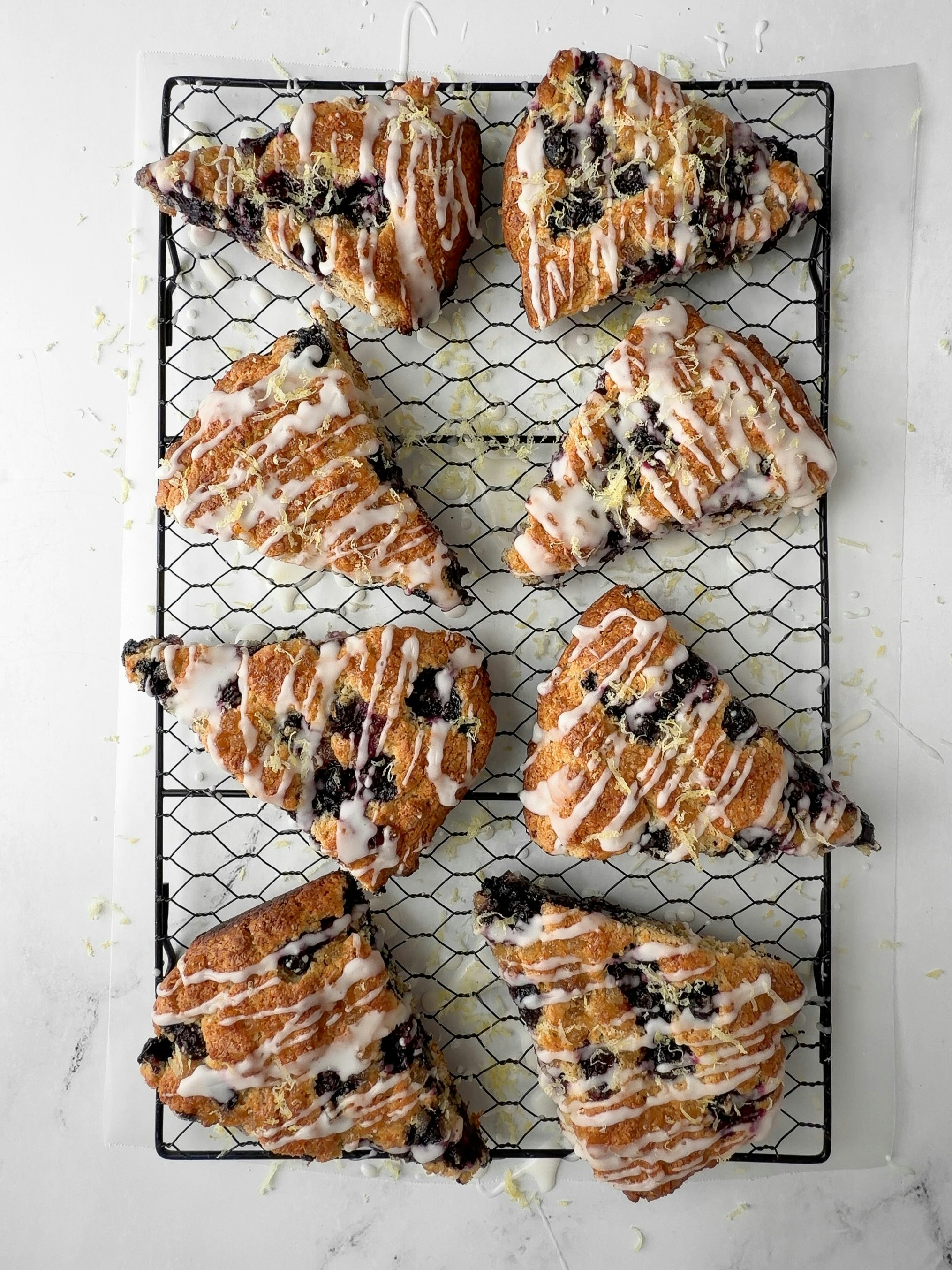 Blueberry scones with white icing on a black cooling rack.