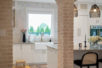 Modern kitchen with white cabinets, farmhouse sink, and brick pillars.