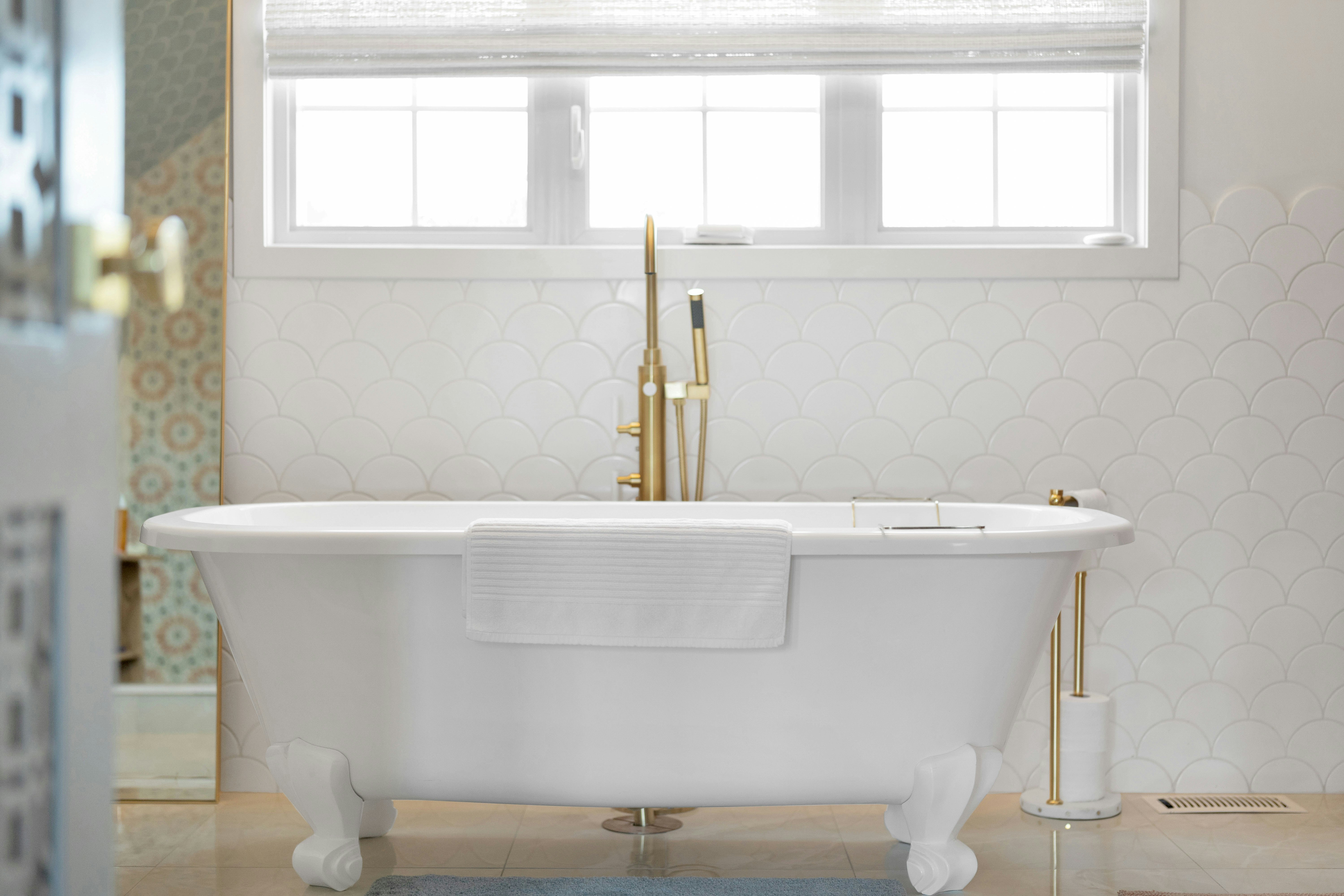 Elegant white clawfoot bathtub with gold fixtures in a bathroom.