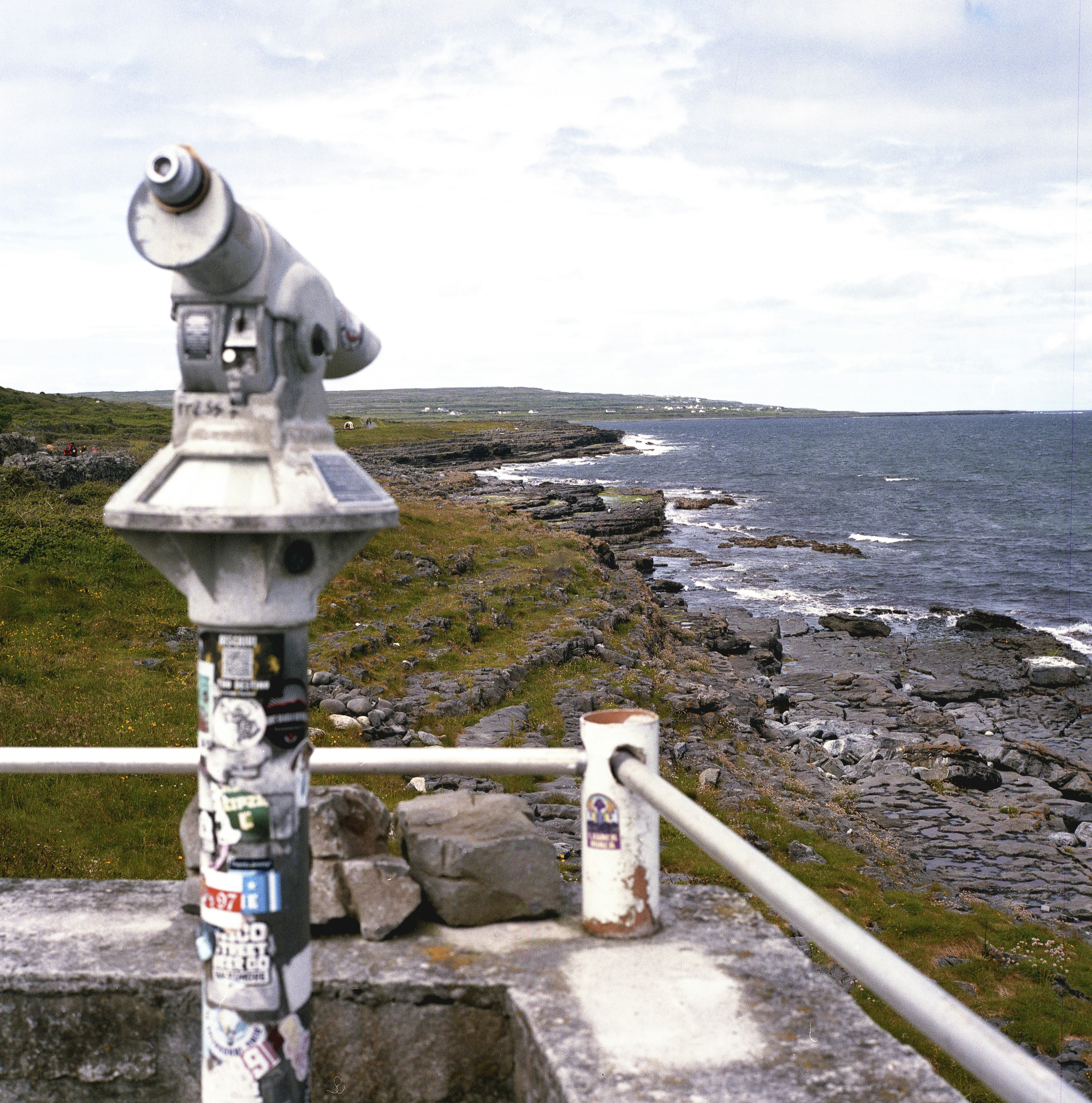 A coin-operated telescope overlooks a rocky coastline and ocean.