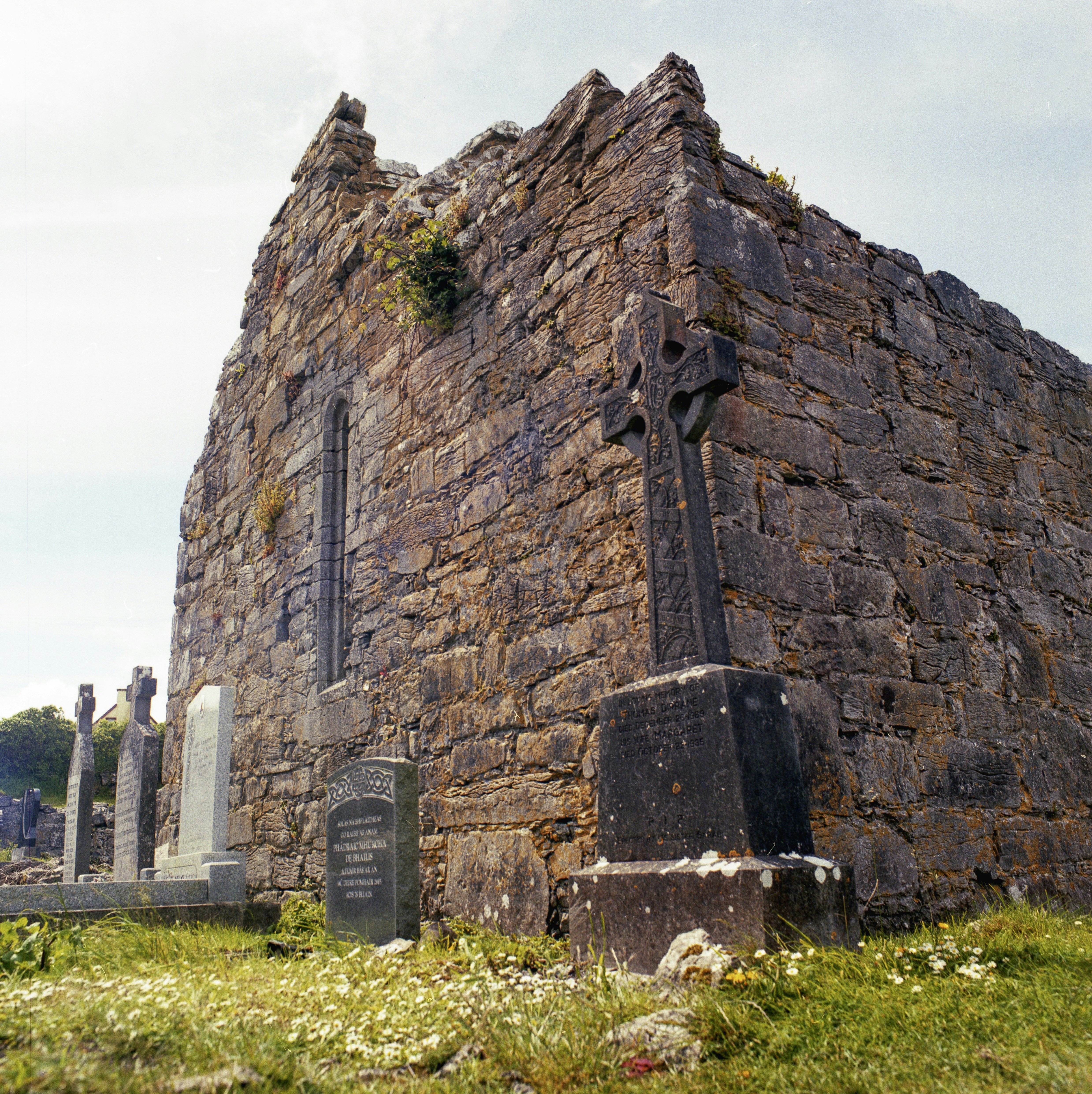 Crumbling stone ruins and a celtic cross in a cemetery.