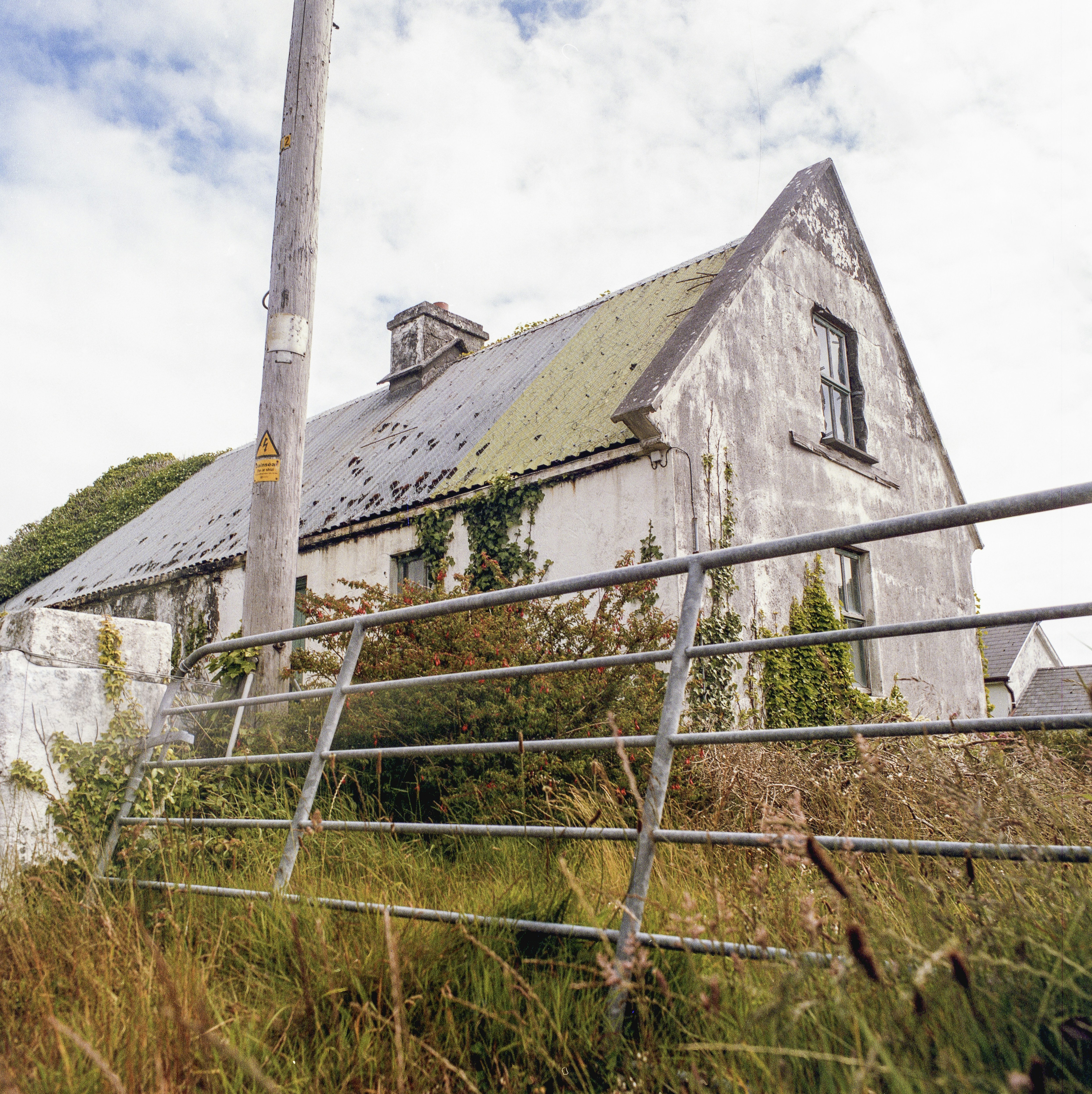 Weathered house behind a metal fence and tall grass.