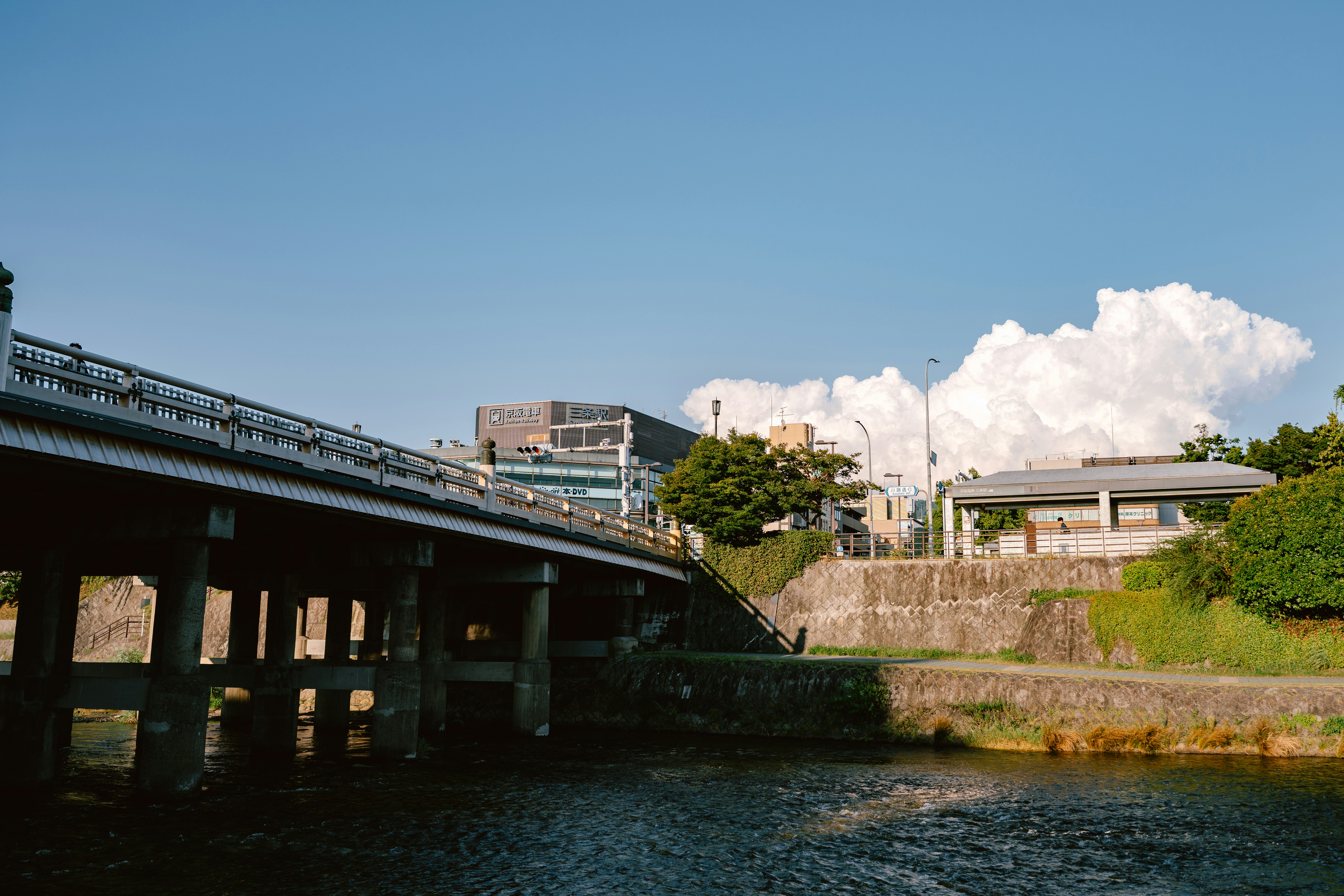 Concrete bridge over river with buildings and blue sky.
