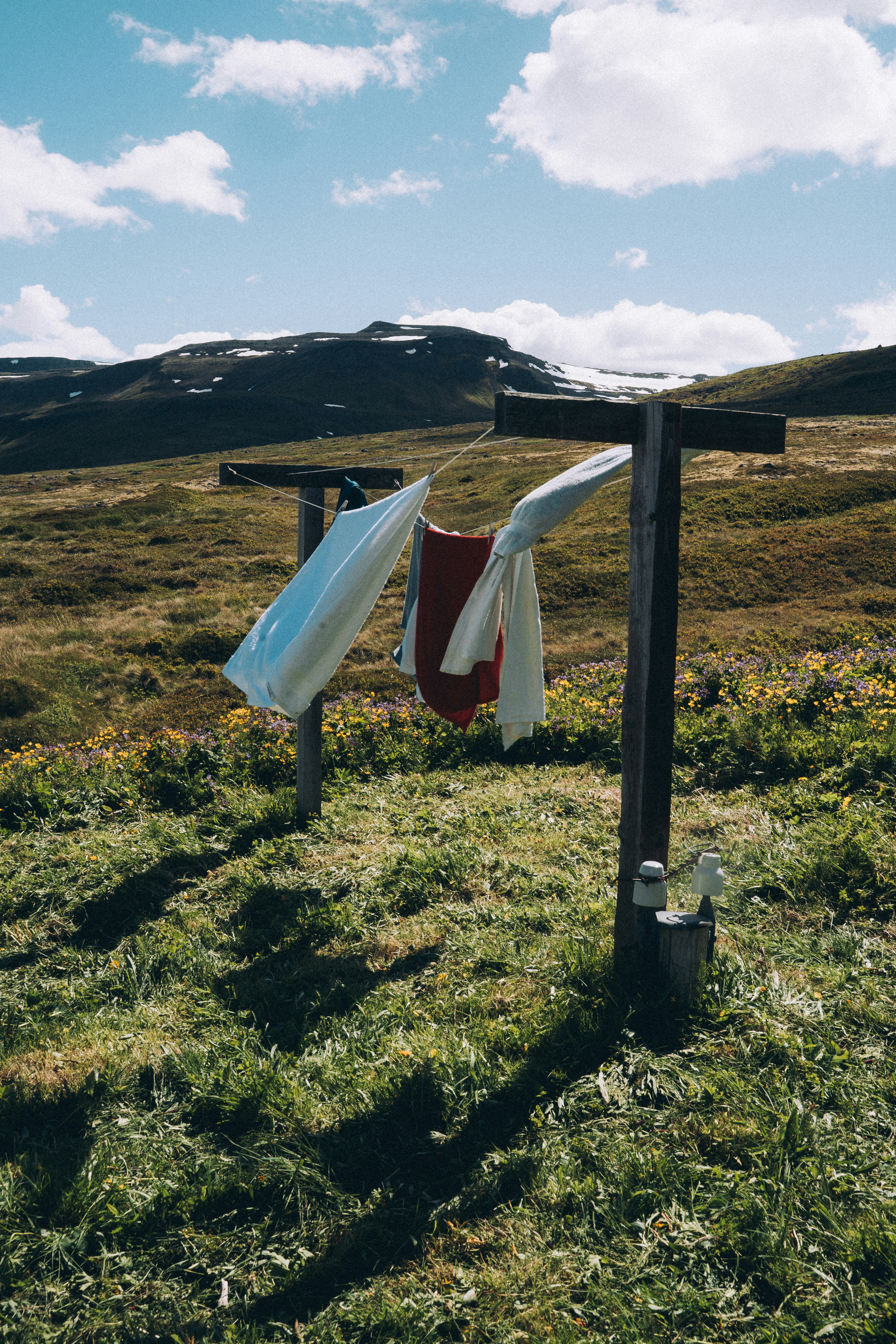 Towels and clothes drying on a metal rack in a grassy upland valley under a blue sky with clouds