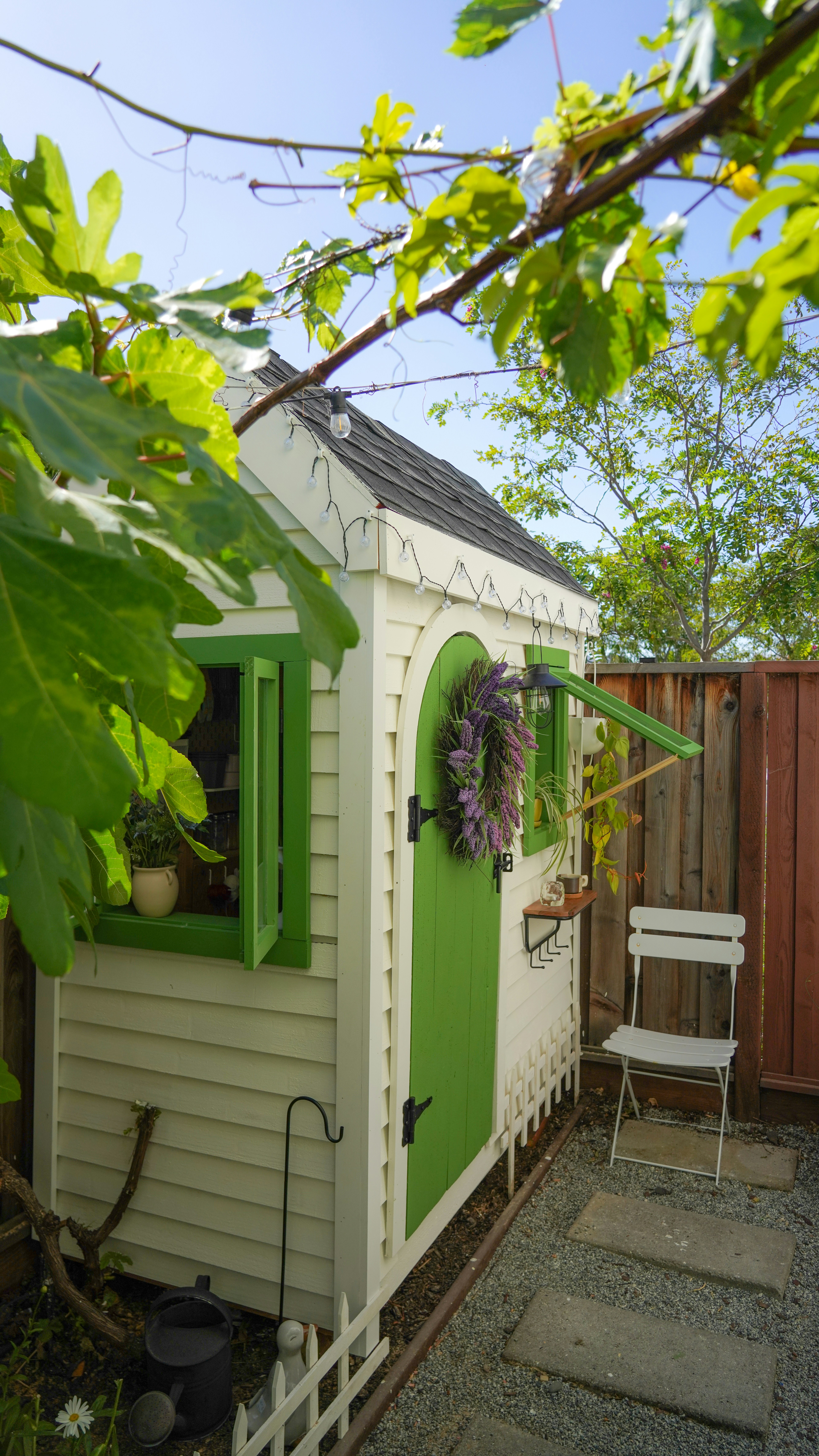 White garden shed with green door and windows.