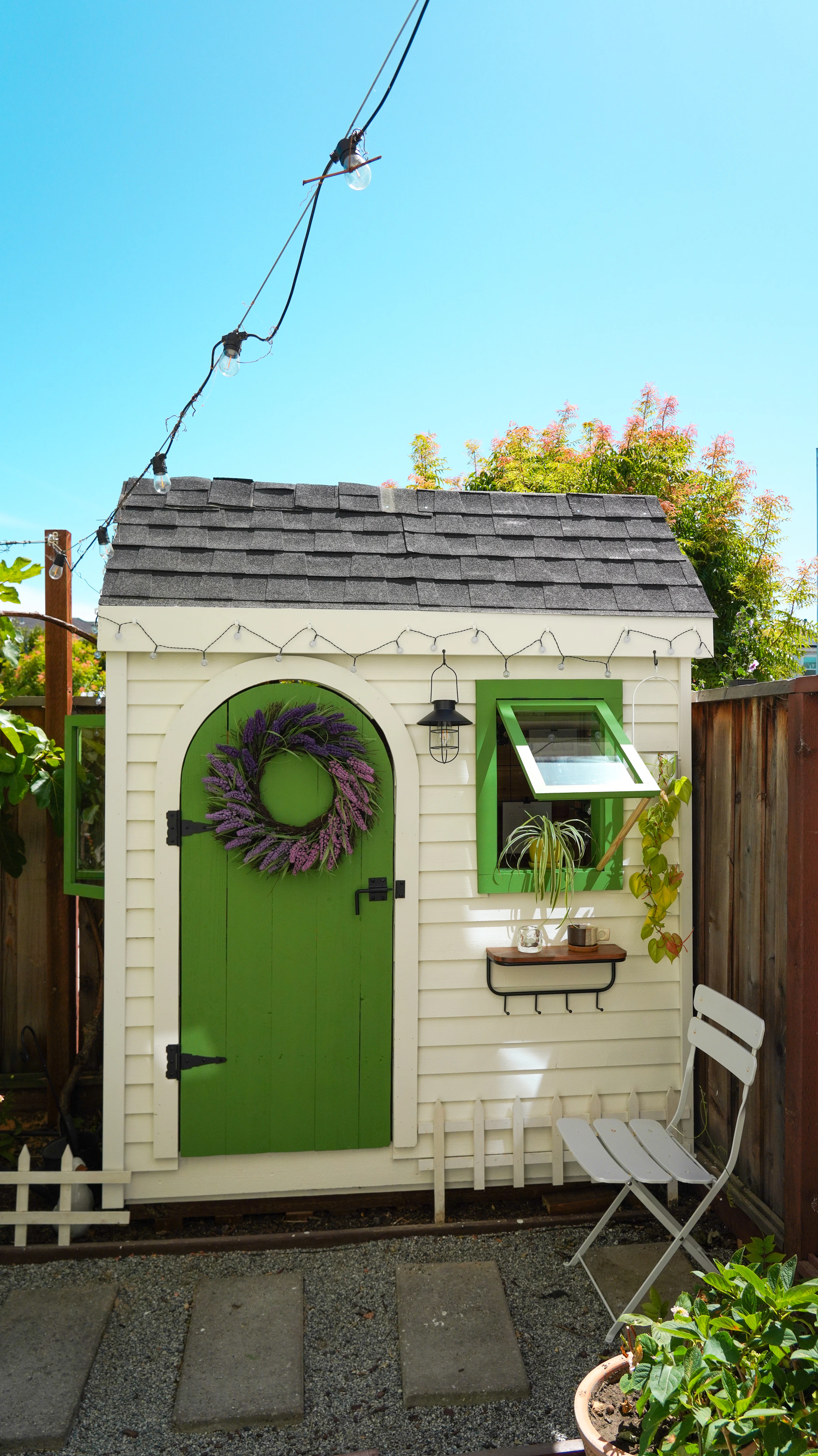 Small white garden building with a green door, open window and plants. Reference photograph; not the project described.