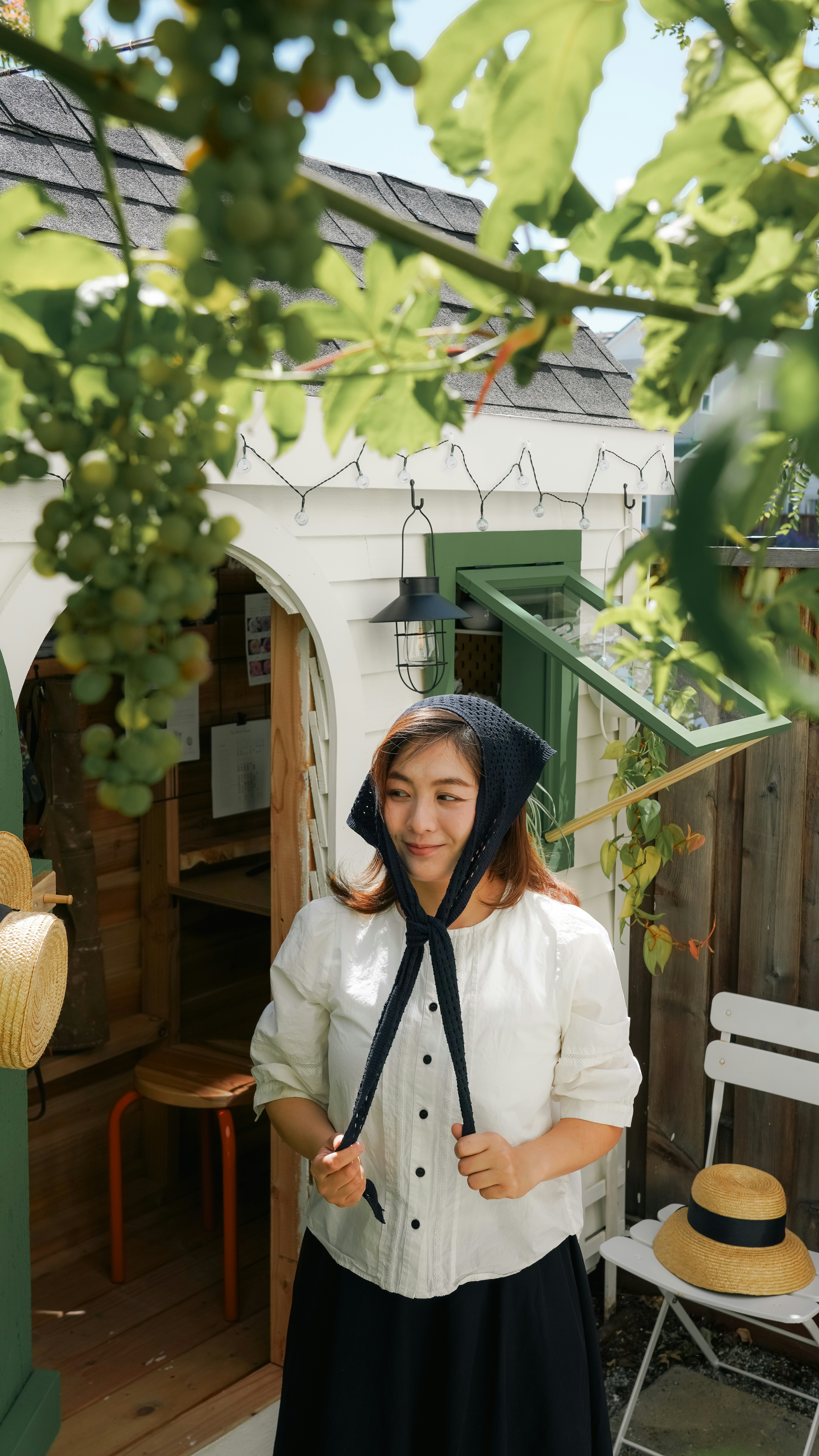 Woman with black headscarf stands among green grapevines.