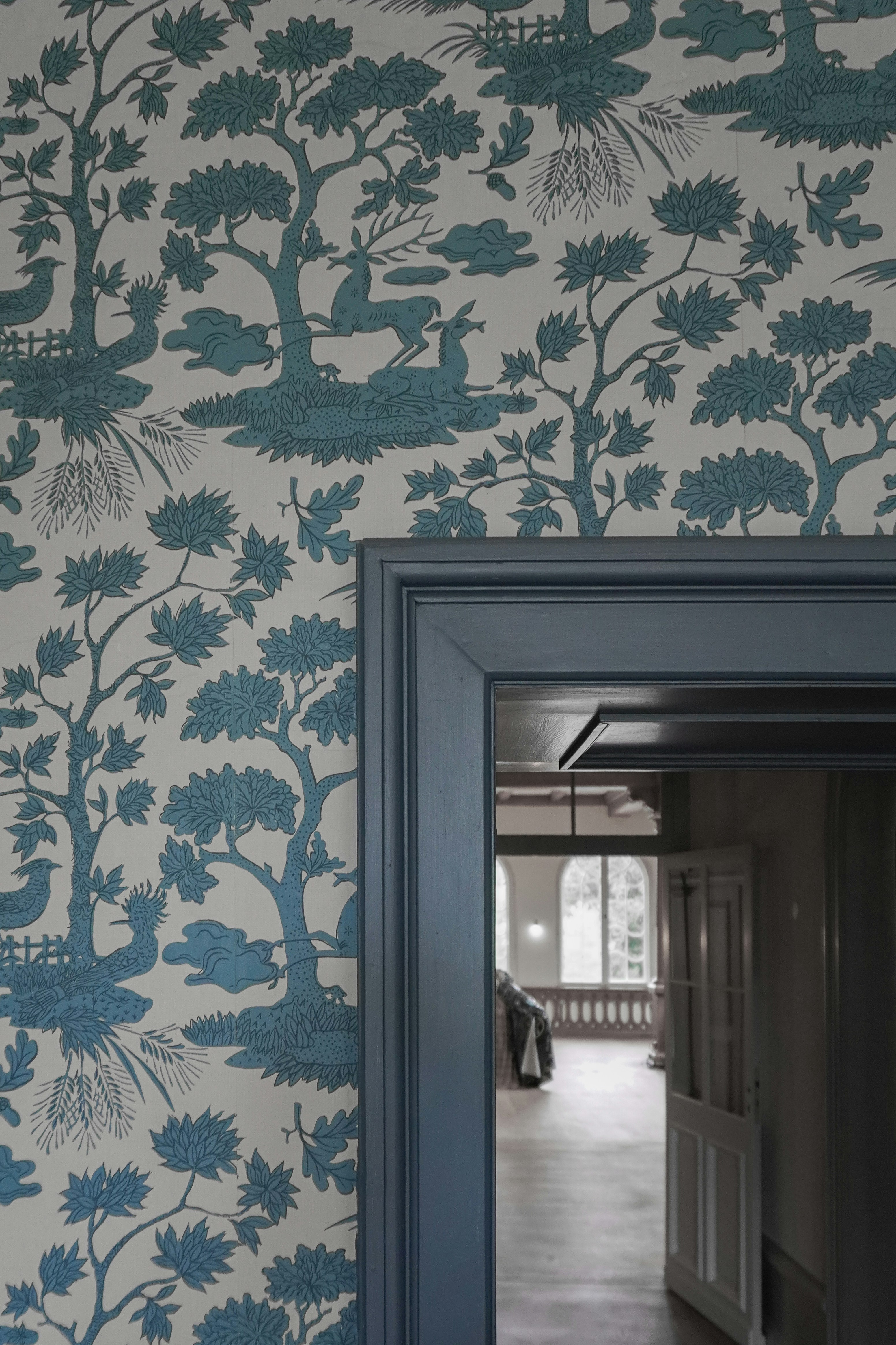 Wallpaper bermotif biru dan putih dengan pohon, rusa, dan burung.