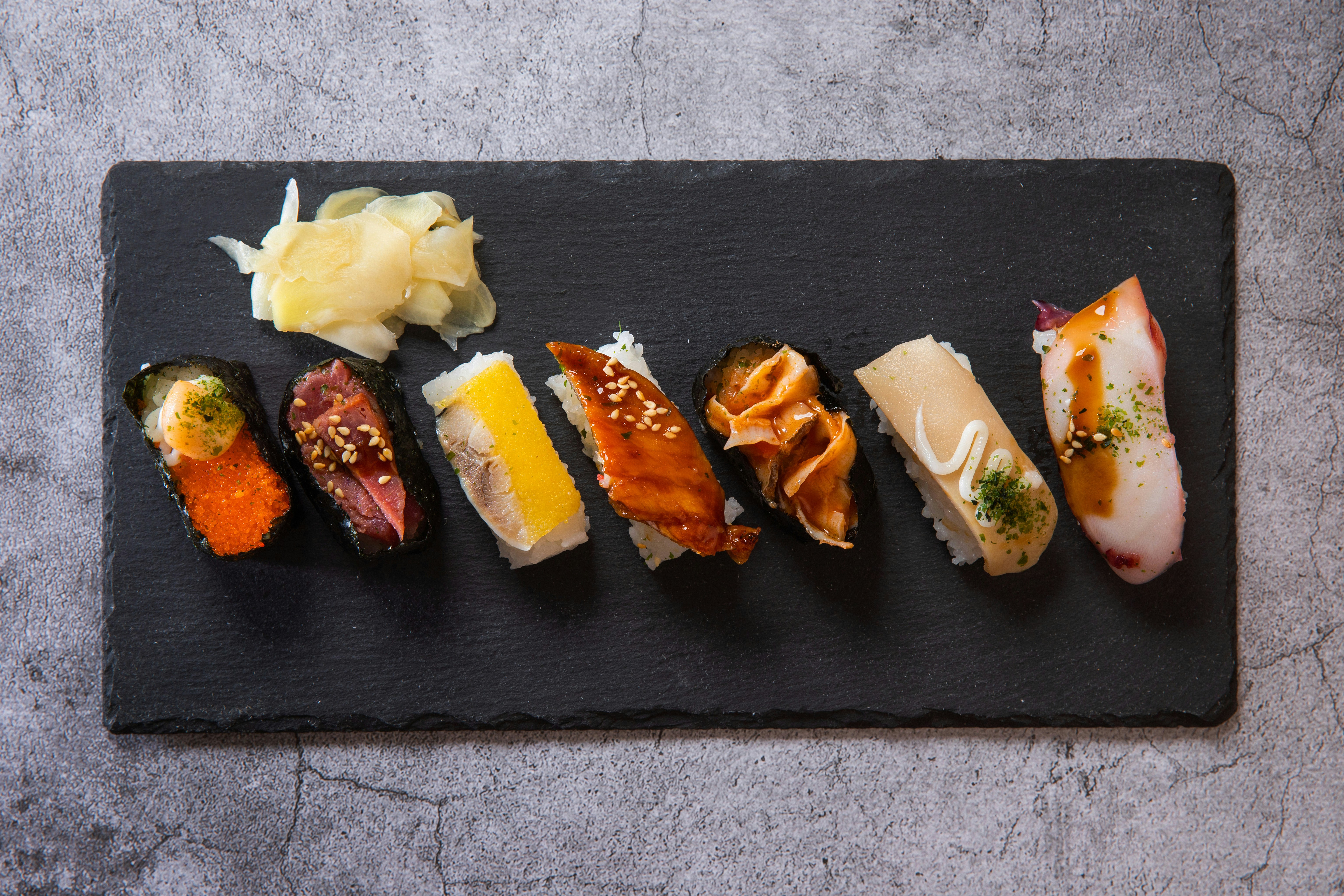Assorted sushi nigiri and pickled ginger on a black plate.