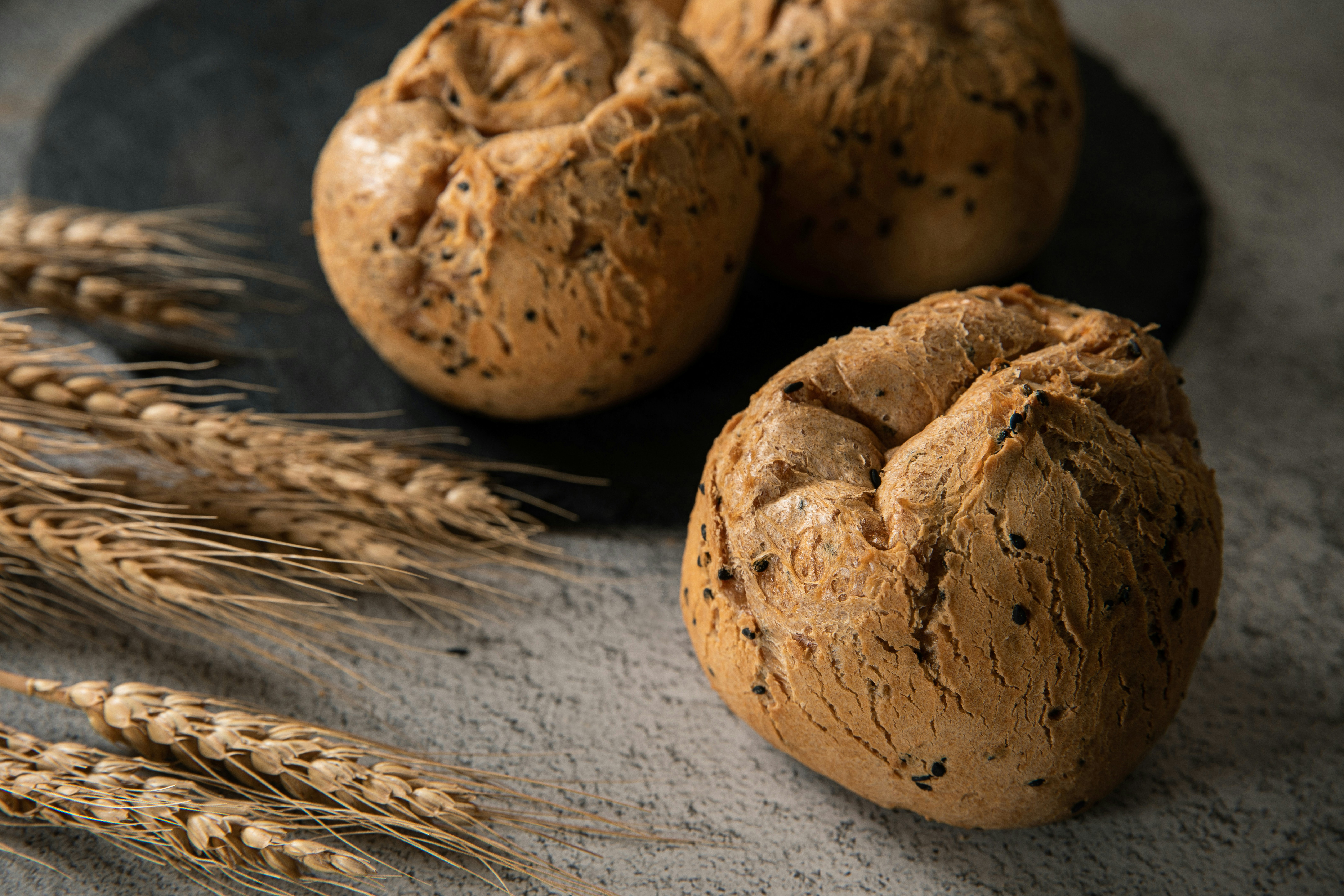 Rustic brown bread rolls beside golden wheat stalks.