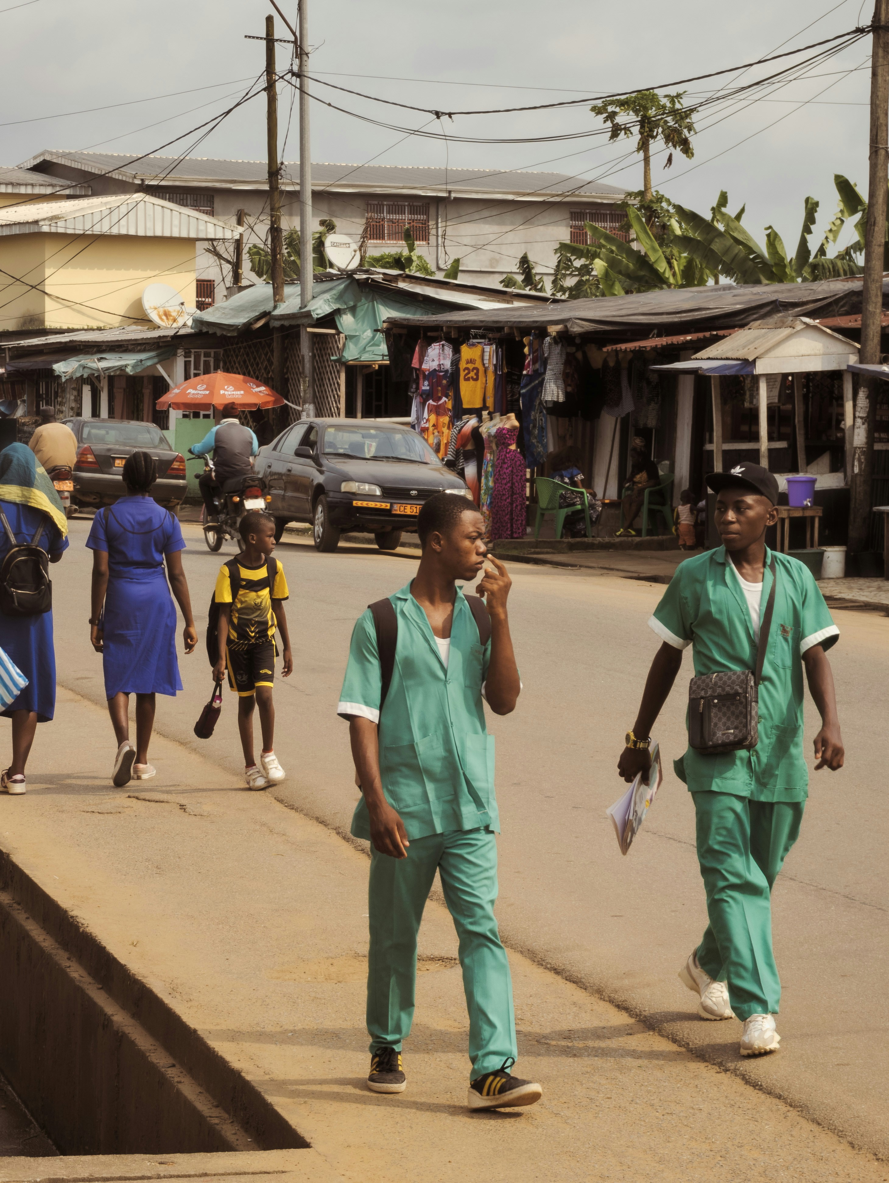 Two men in green scrubs walk along a busy street.